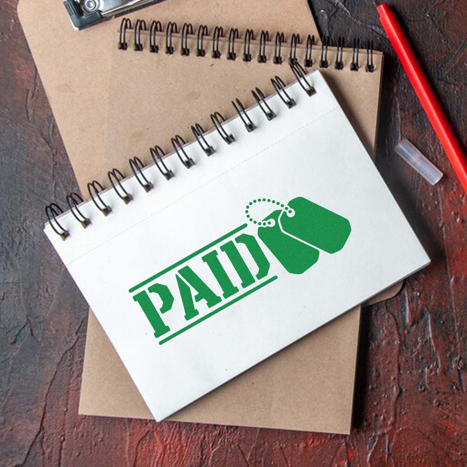 Green PAID rubber stamp on spiral notebook for invoices, document approval, and office bookkeeping.