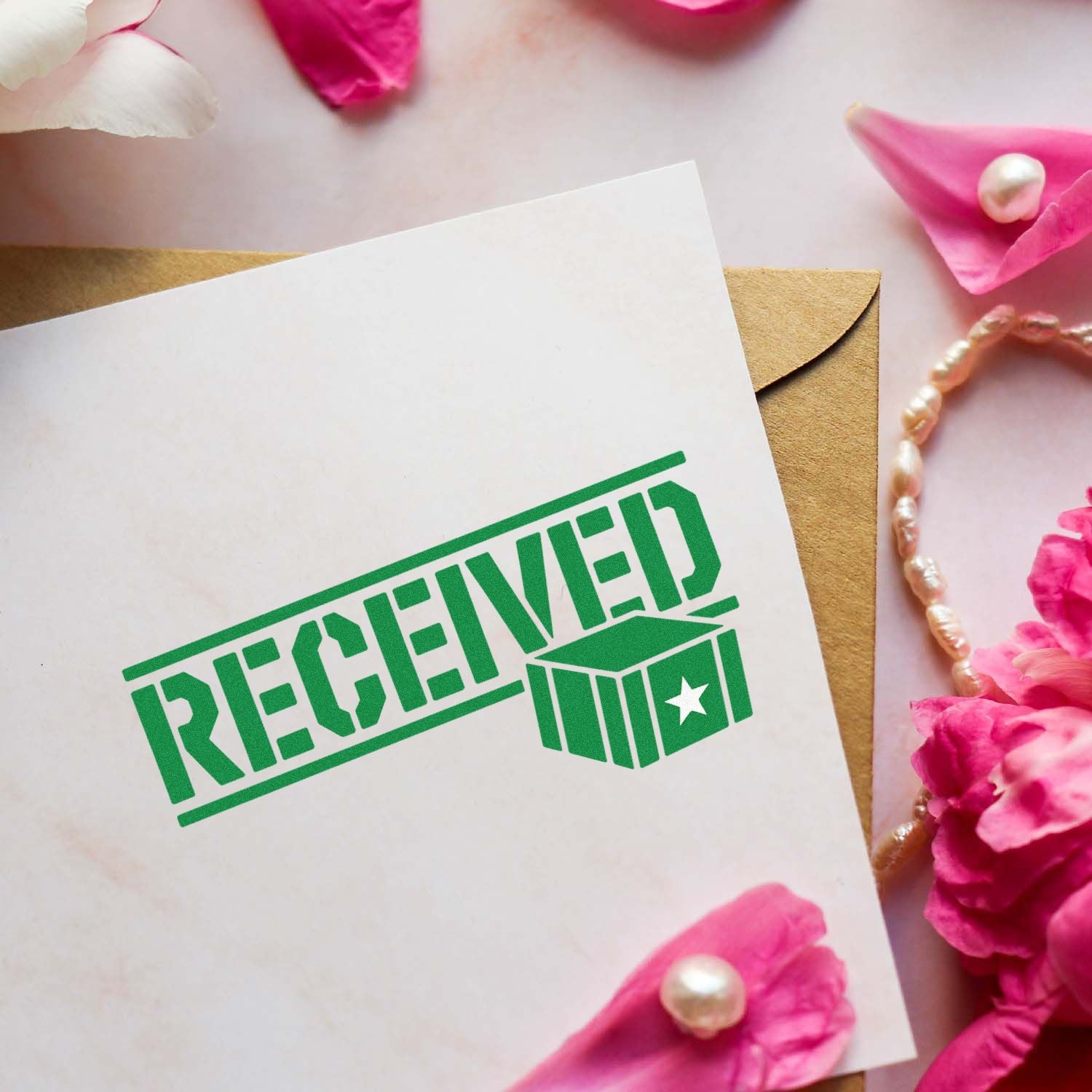 Green RECEIVED rubber stamp on white card over kraft envelope, styled with pink petals for stationery packaging.