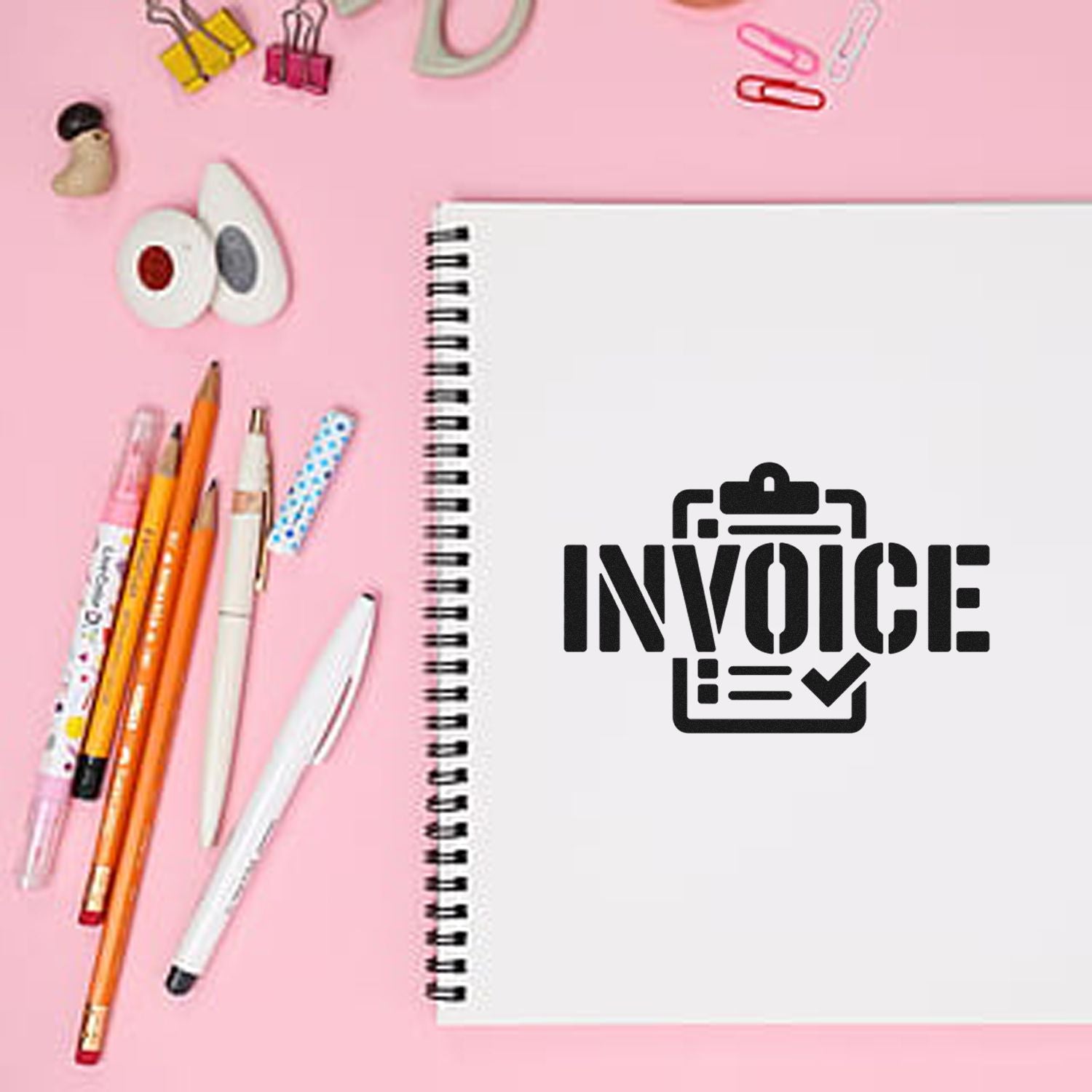 Invoice rubber stamp design on spiral notebook with pens on pink desk for office and accounting use