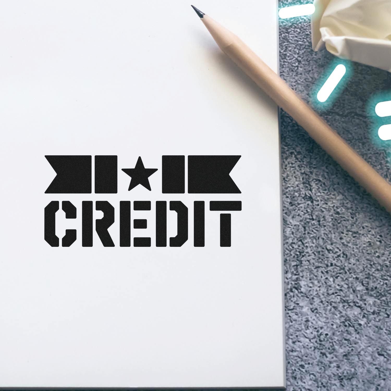 MKT CREDIT custom rubber stamp impression on notebook beside a pencil, showing branded stationery design.