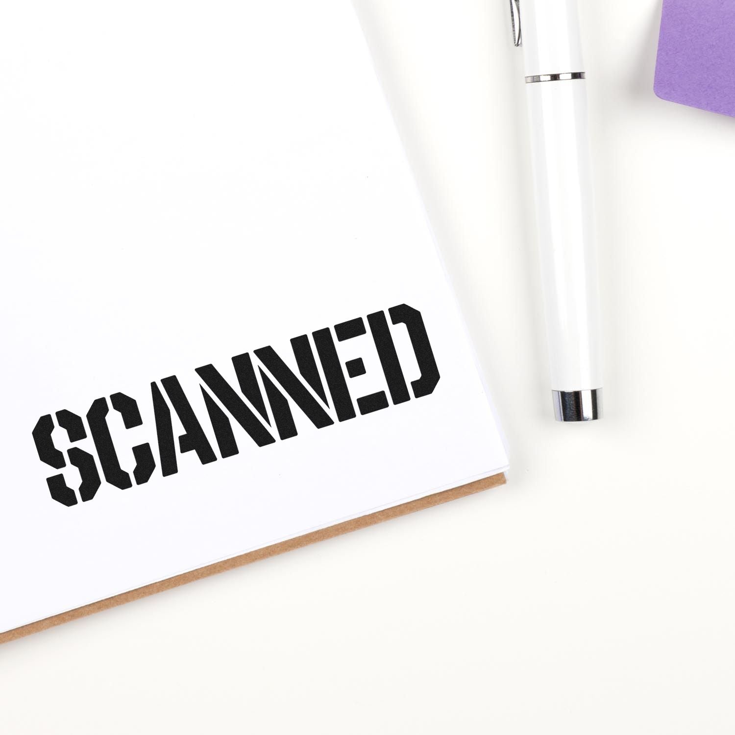 Rubber stamp imprint reading SCANNED on a notebook page with pen, marking a document as scanned.