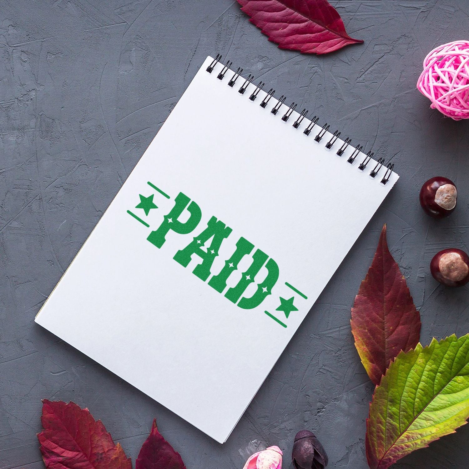 Green PAID rubber stamp on spiral notebook, marking completed payment for office invoicing and accounting use.