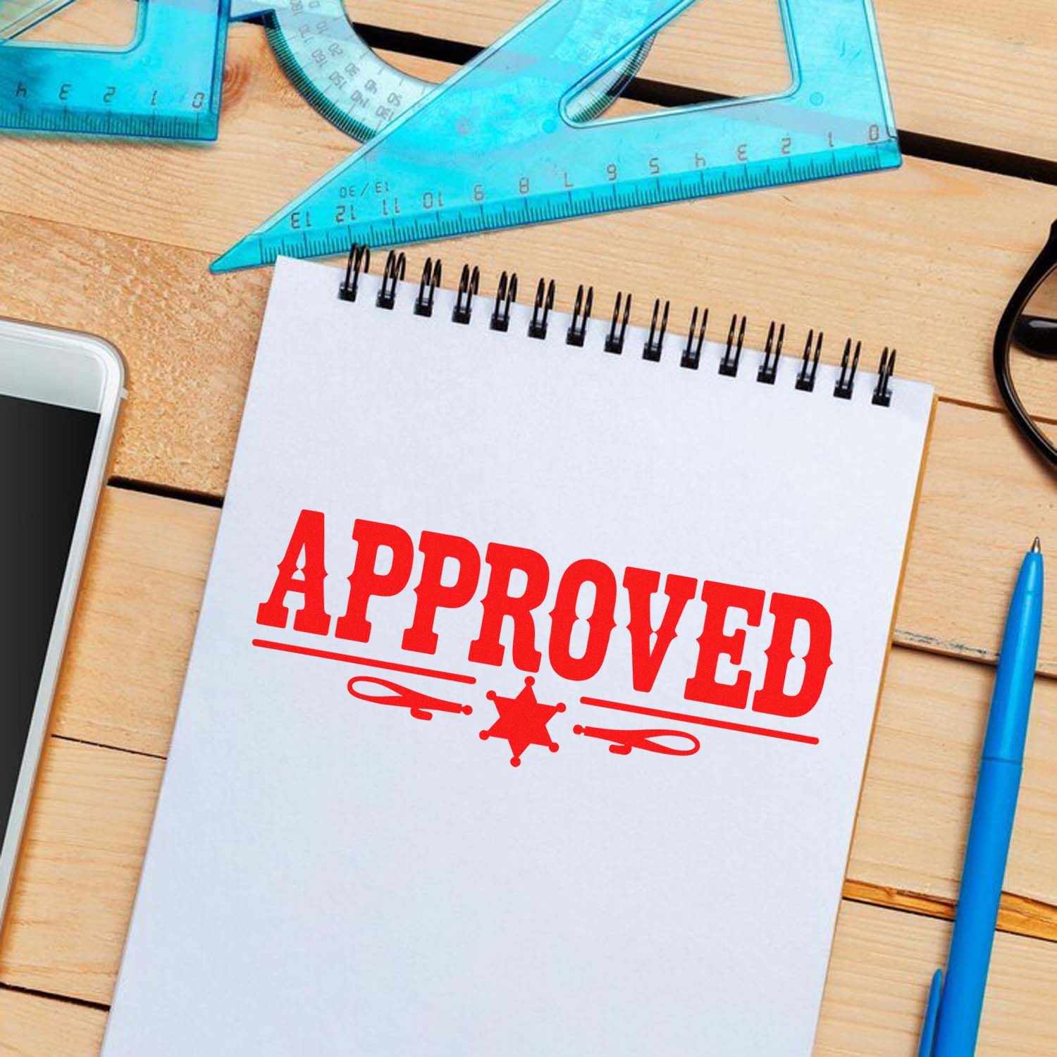 Approved rubber stamp impression on notebook with rulers and pen, for document approval and office use.