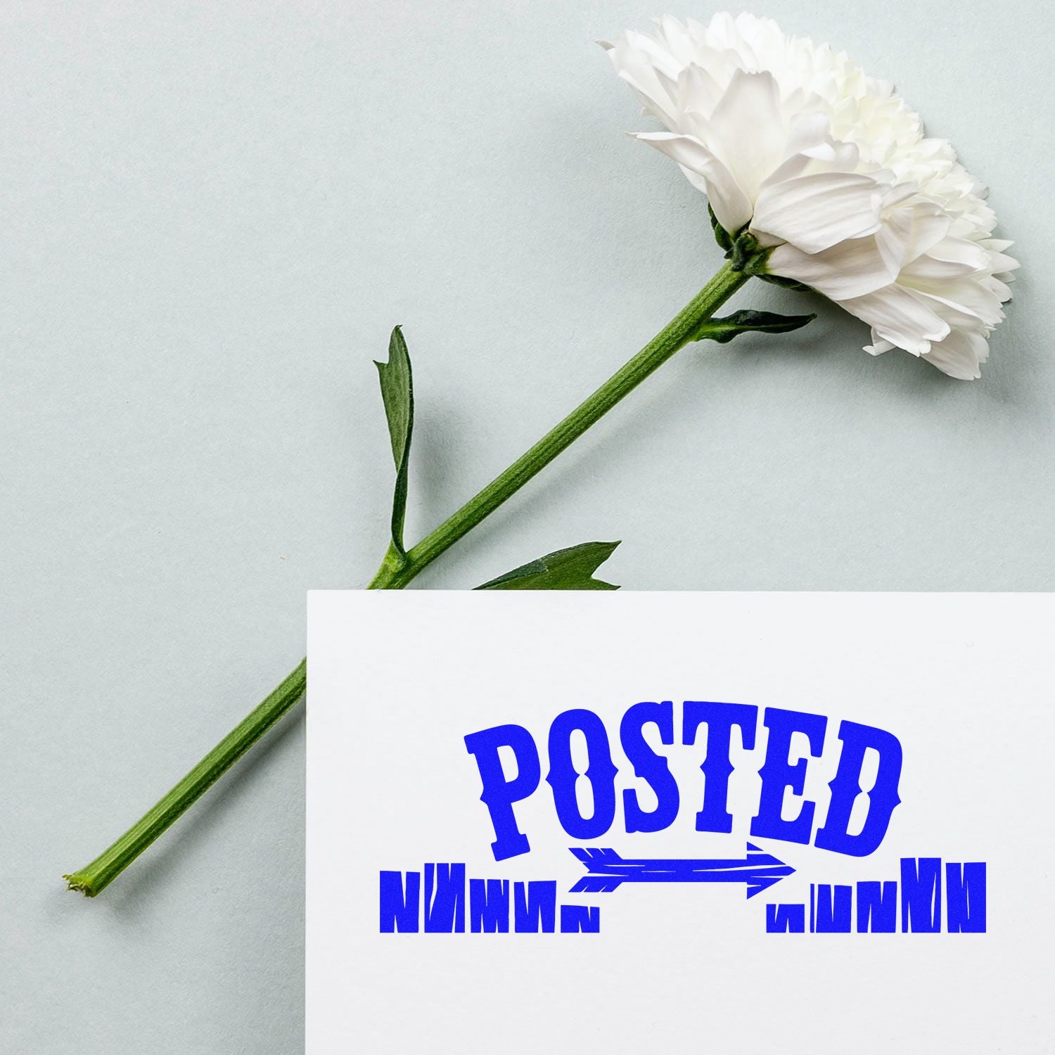 Blue Posted rubber stamp on card beside white flower for custom stationery and mailing branding.