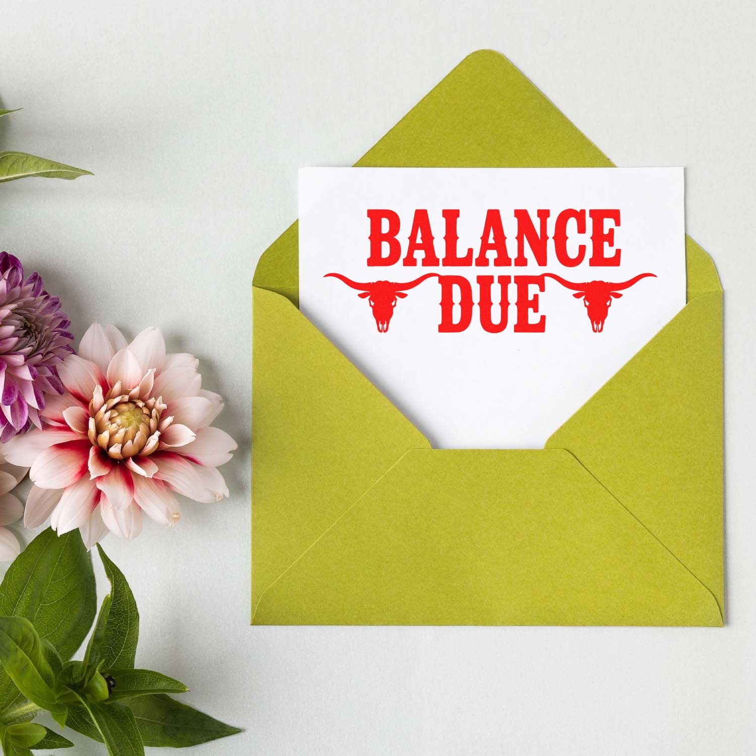 Balance Due rubber stamp with red longhorn skull design on a card inside a green envelope.