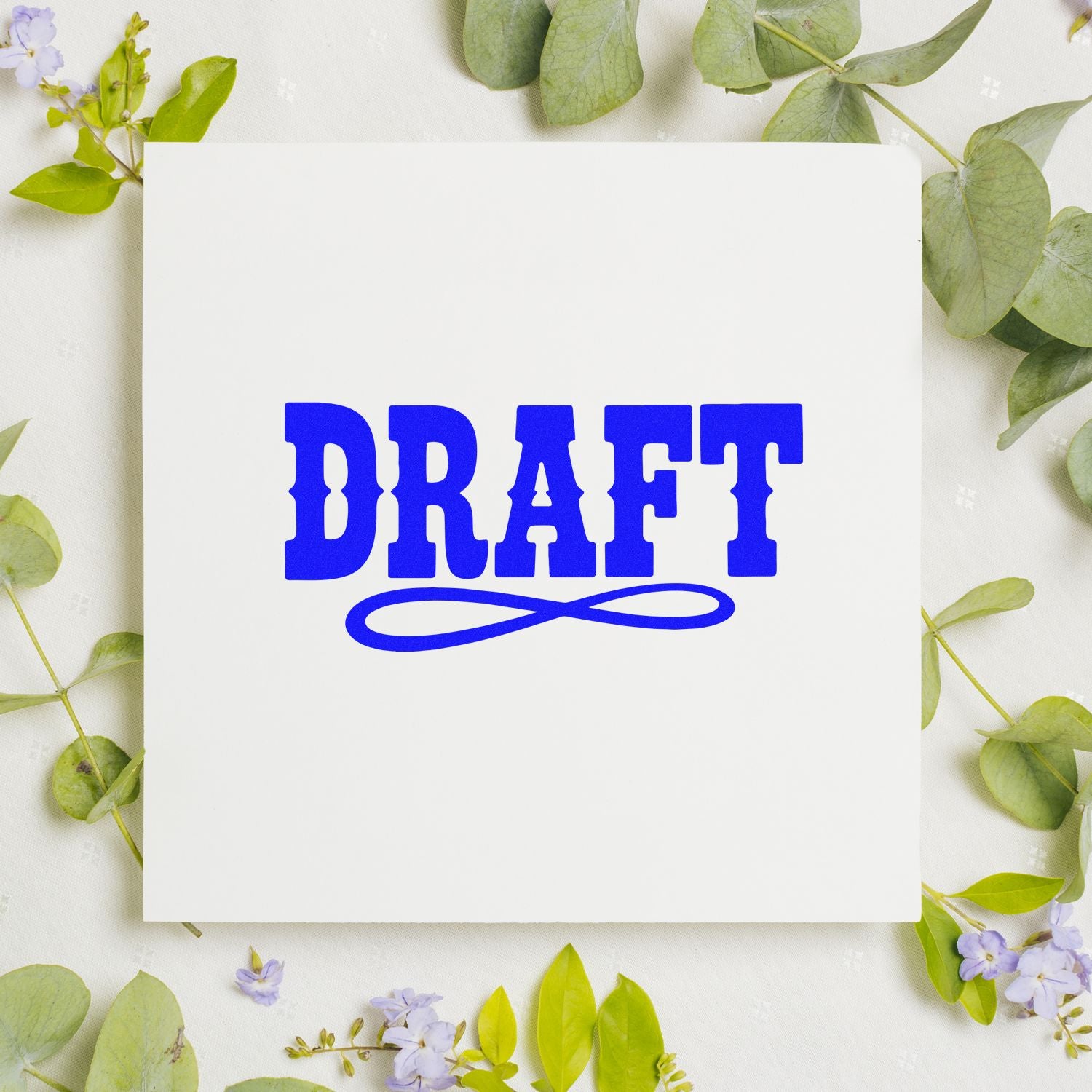 Blue DRAFT rubber stamp design on a white card, surrounded by greenery and flowers, for marking documents as drafts.