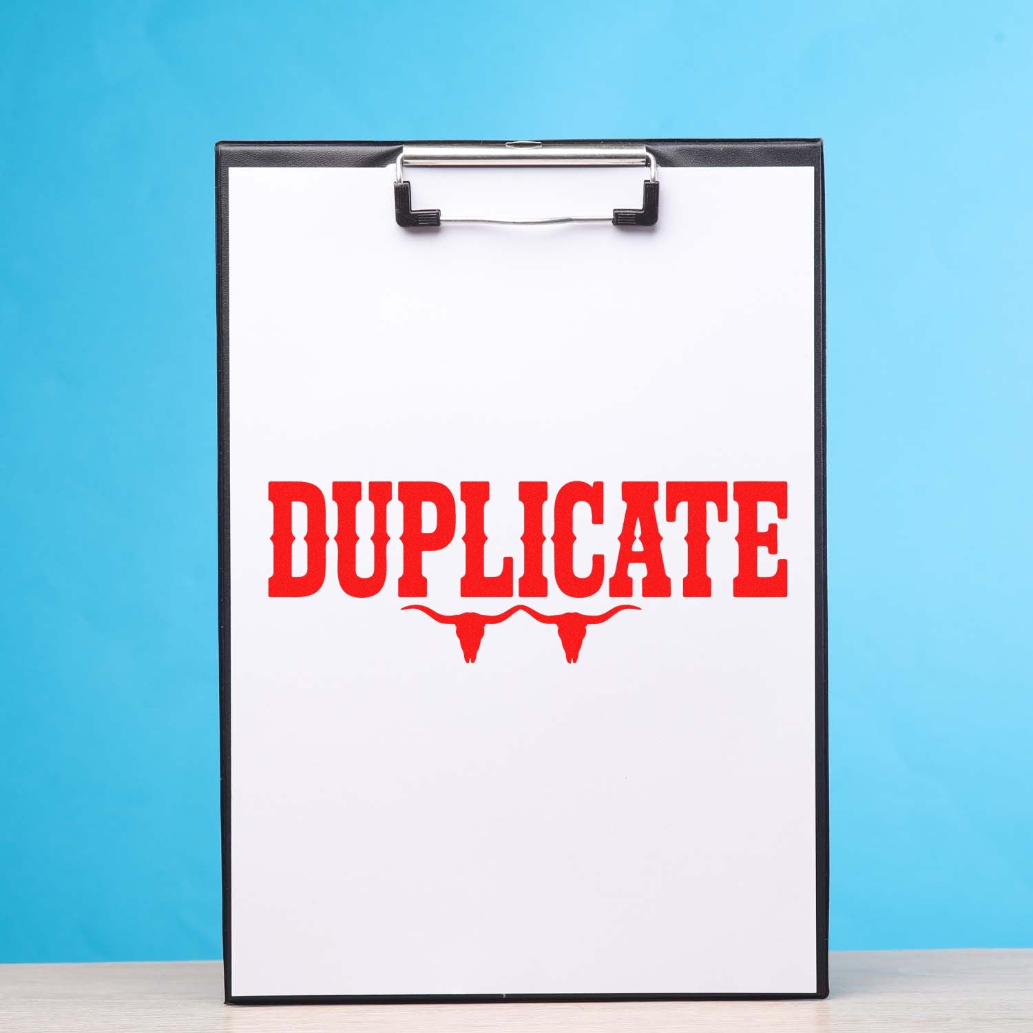 Red duplicate rubber stamp imprint on clipboard for marking office documents.