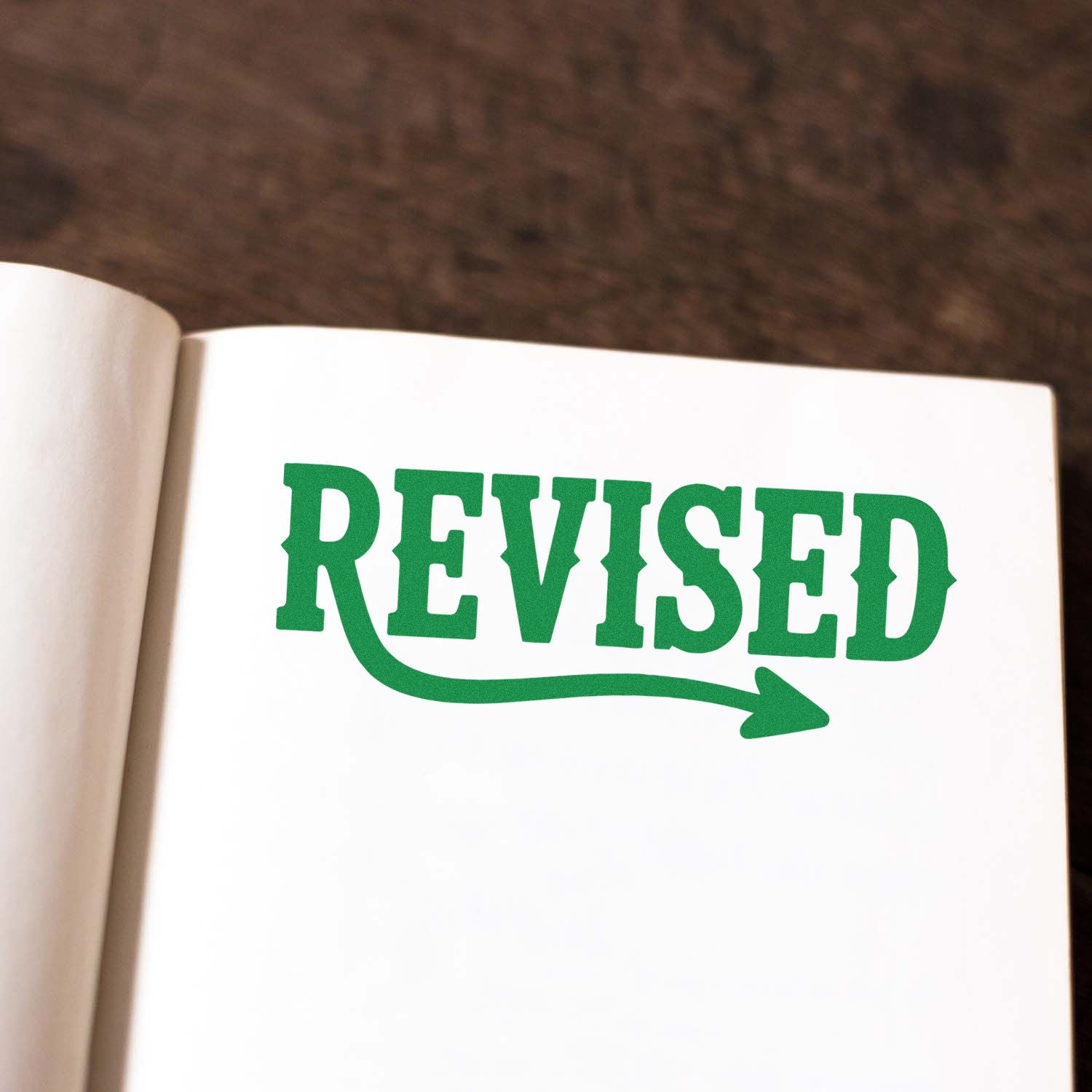 Green REVISED rubber stamp on notebook page with arrow underline, ideal for editing, proofing, and document approval.