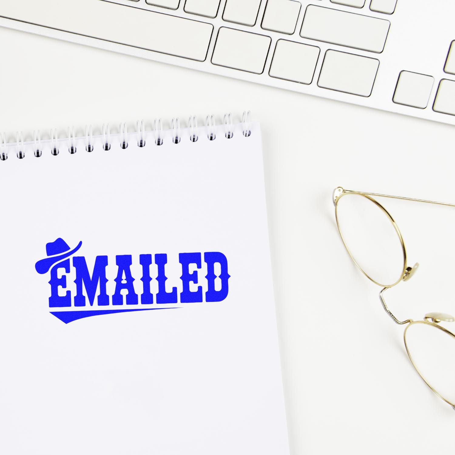 Custom blue EMAILED rubber stamp on notebook for office mail tracking beside keyboard and glasses