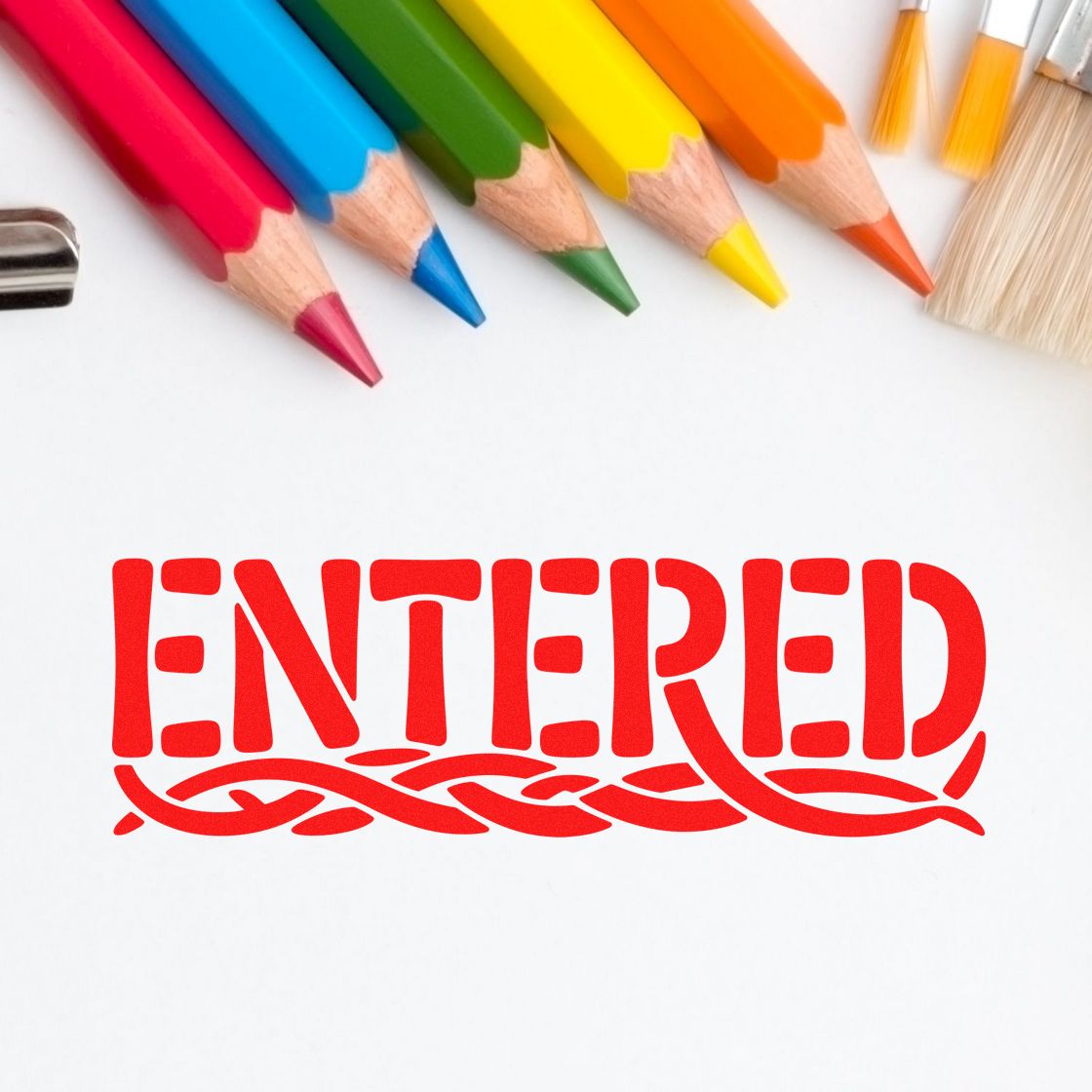 Red ENTERED rubber stamp impression on paper, framed by colored pencils and brushes for office approval marking.