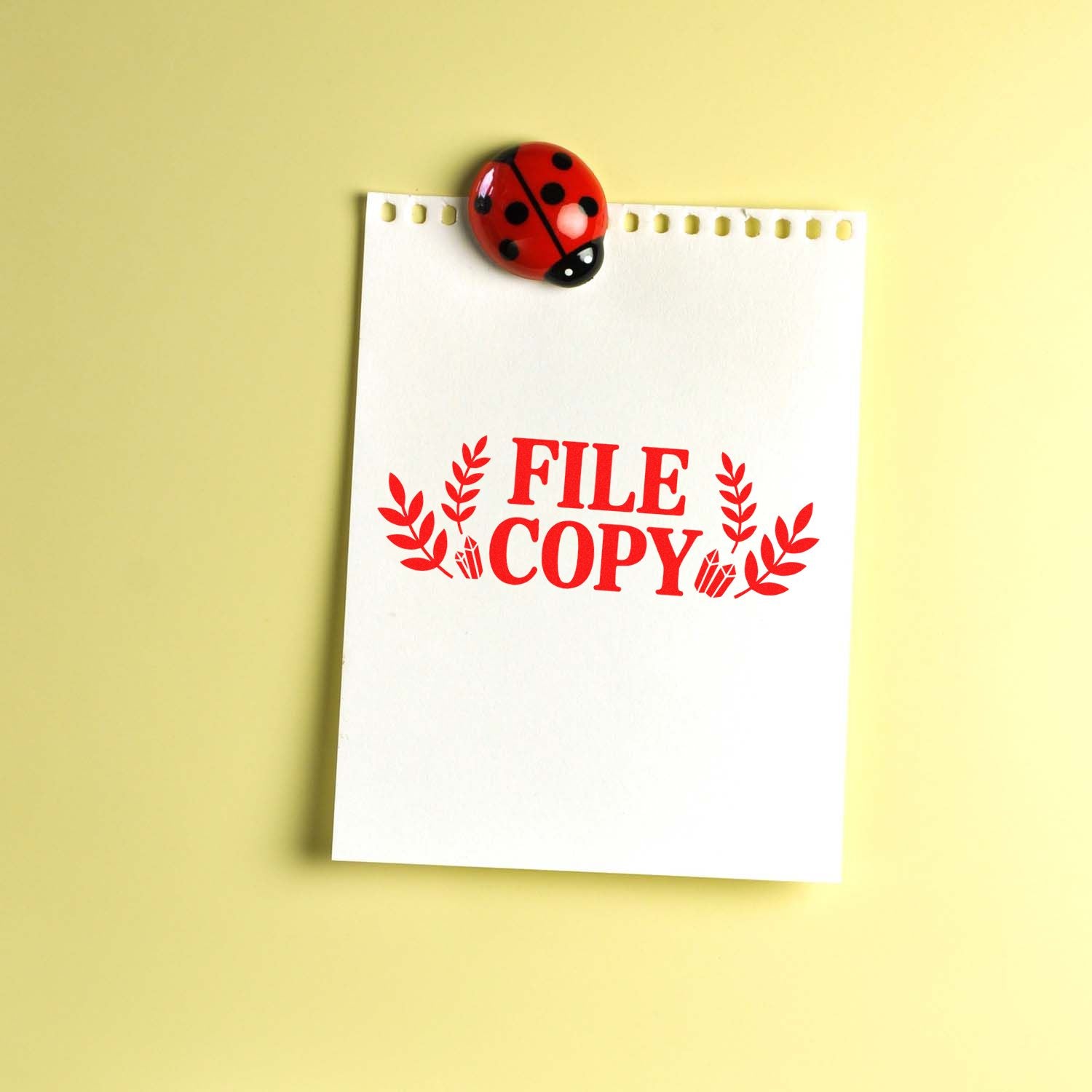 File copy rubber stamp on notepad, pinned with a ladybug clip on yellow background for office document organization.