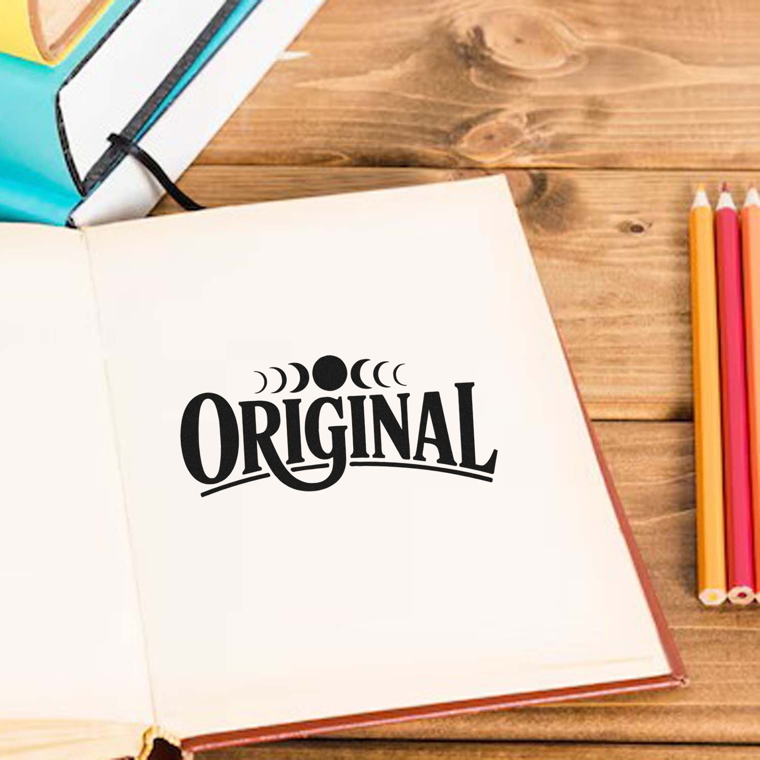 Original rubber stamp impression on an open notebook, featuring a moon phase design and stationery on a wooden desk.