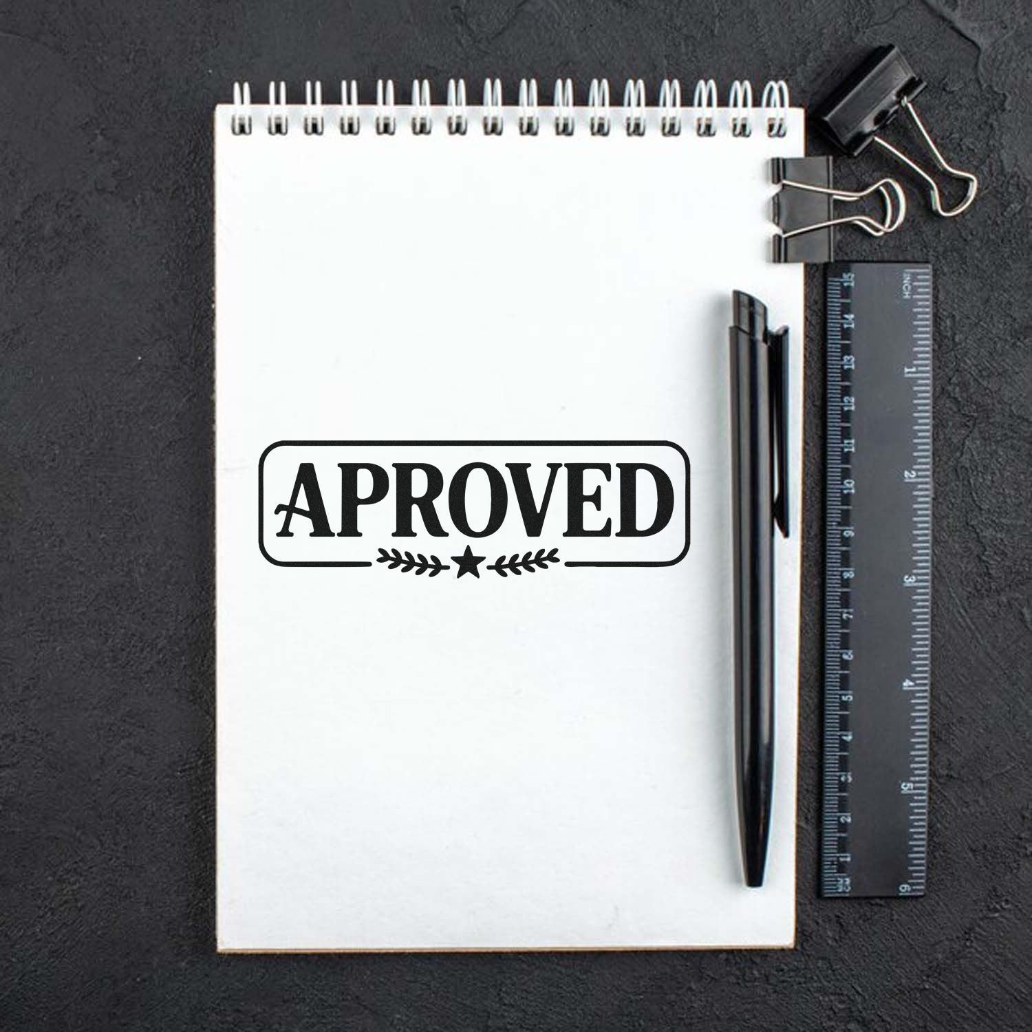 Approved rubber stamp imprint on notepad with pen and ruler for office document marking.