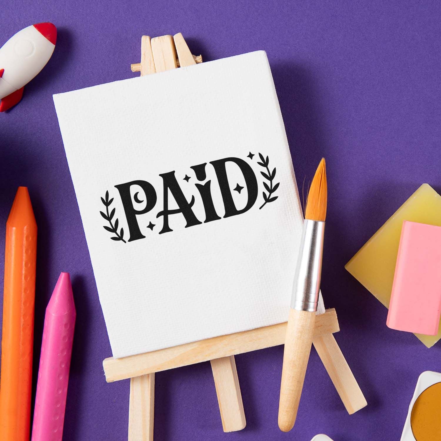 Paid rubber stamp on easel with craft supplies, ideal for marking invoices and business documents.