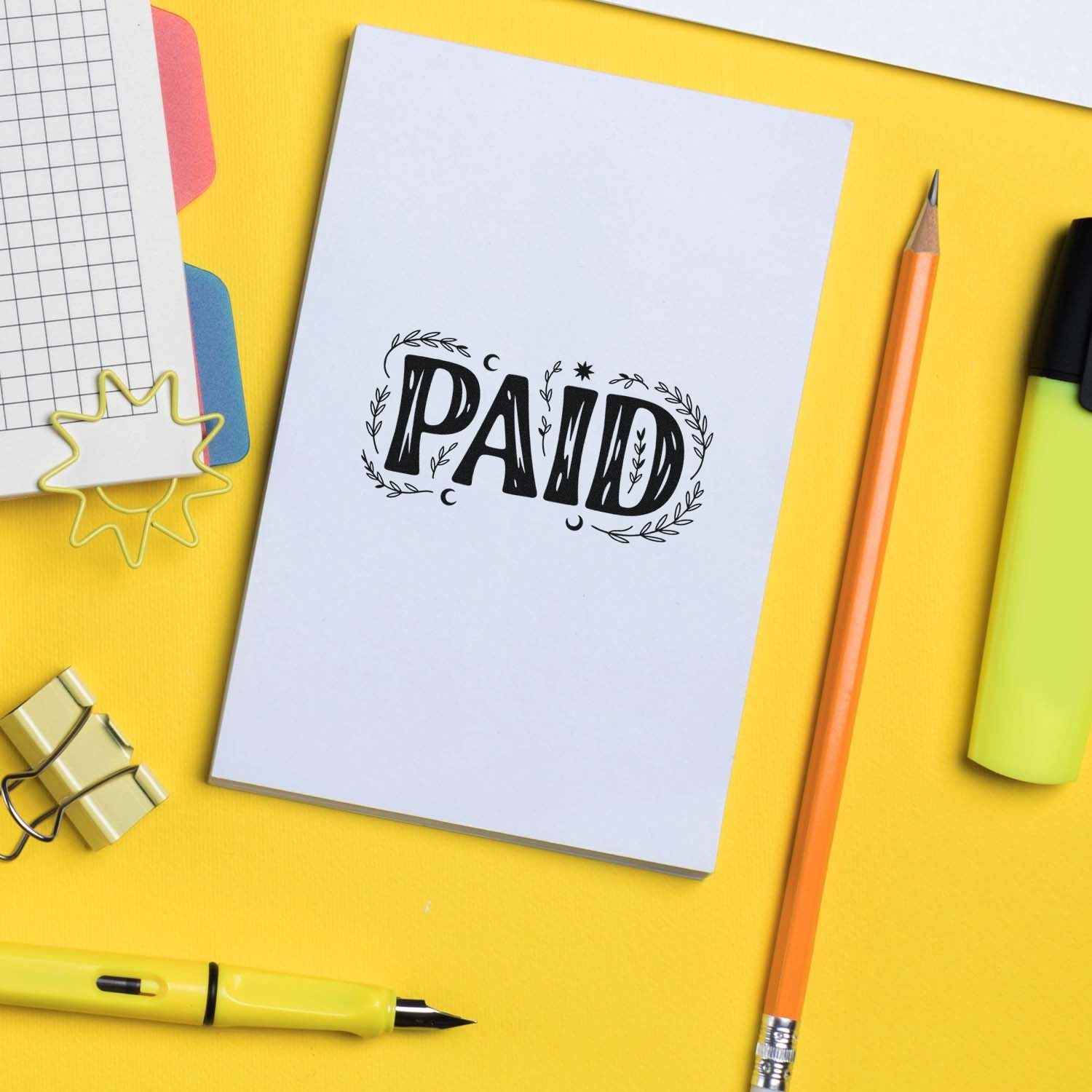 PAID rubber stamp impression on notebook page with stationery, ideal for office accounting and business document marking.