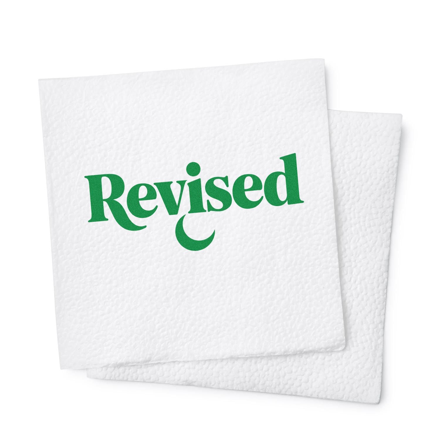 Green Revised rubber stamp on stacked white paper, used to mark updated documents and forms.
