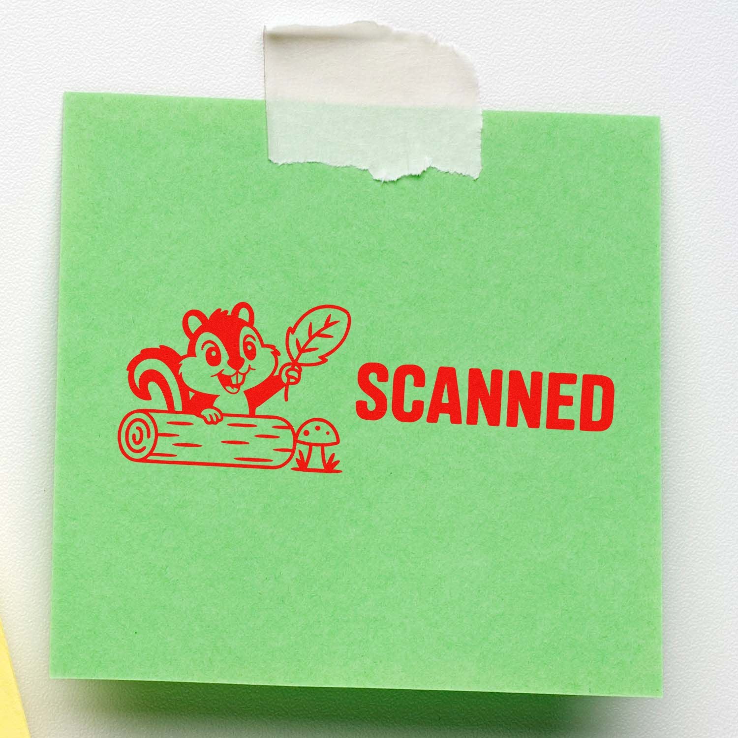 Red scanned rubber stamp of a cartoon squirrel holding a leaf on a log, printed on a green sticky note.
