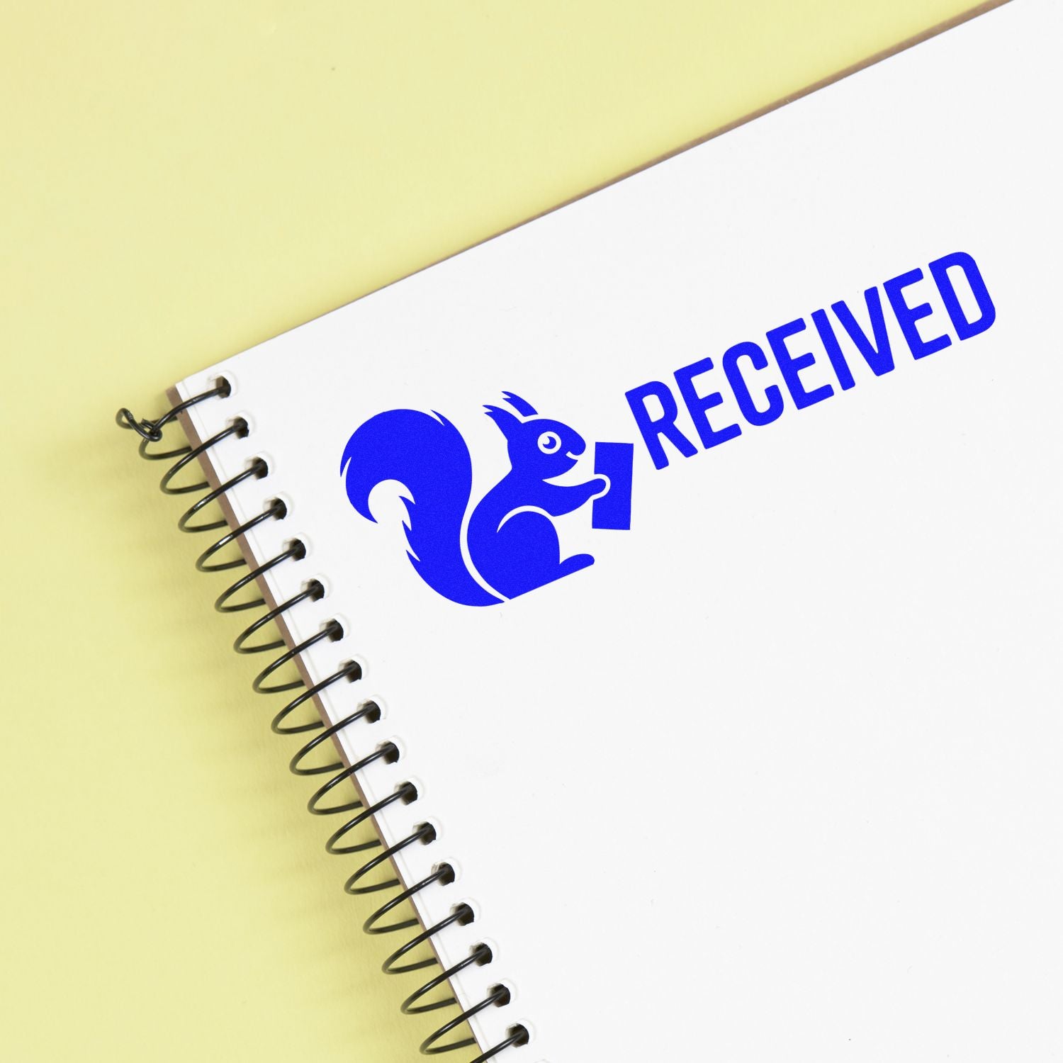 Blue RECEIVED rubber stamp imprint with squirrel logo on a spiral notebook, ideal for office document processing.