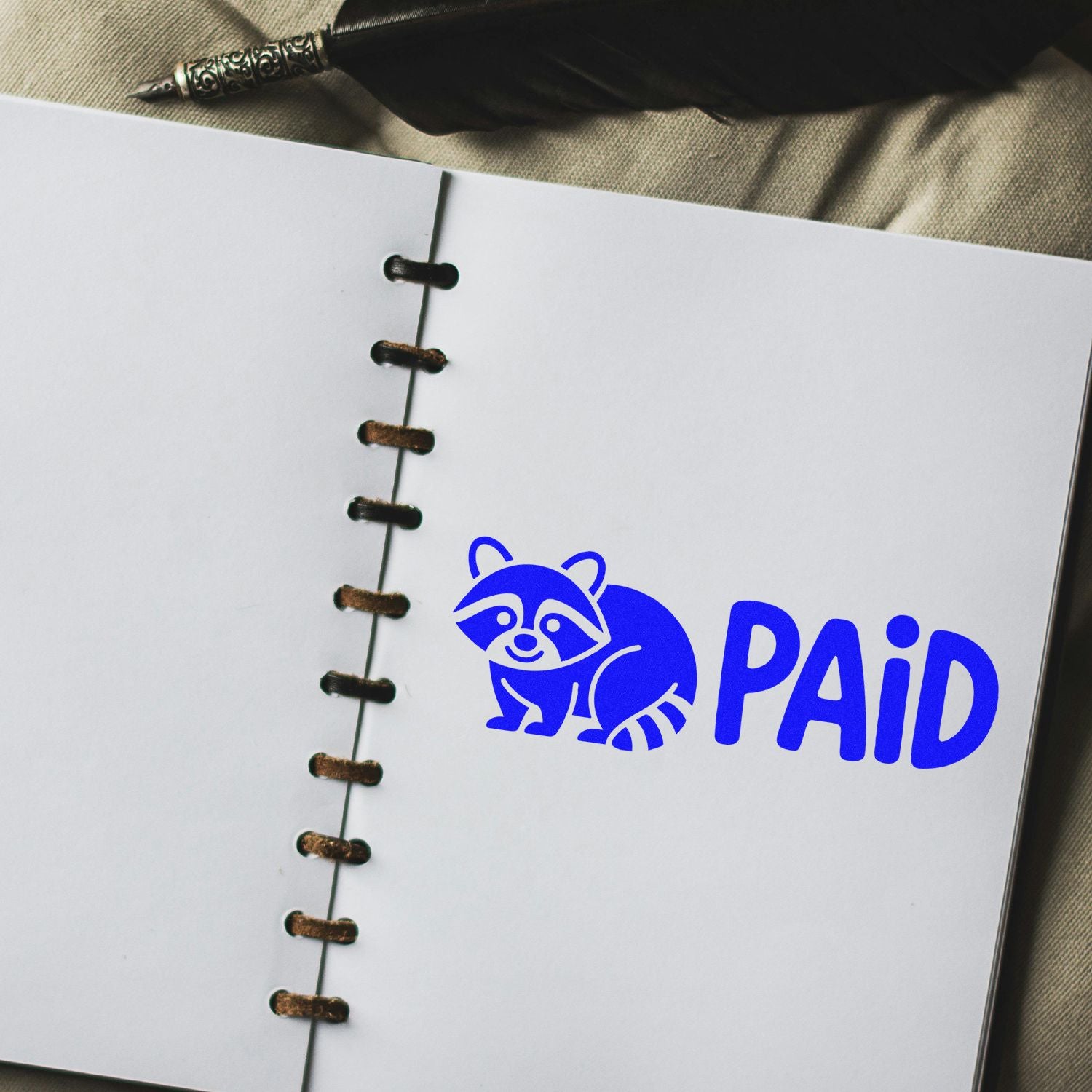 Blue PAID rubber stamp with raccoon icon on notebook page for custom business bookkeeping stamps.