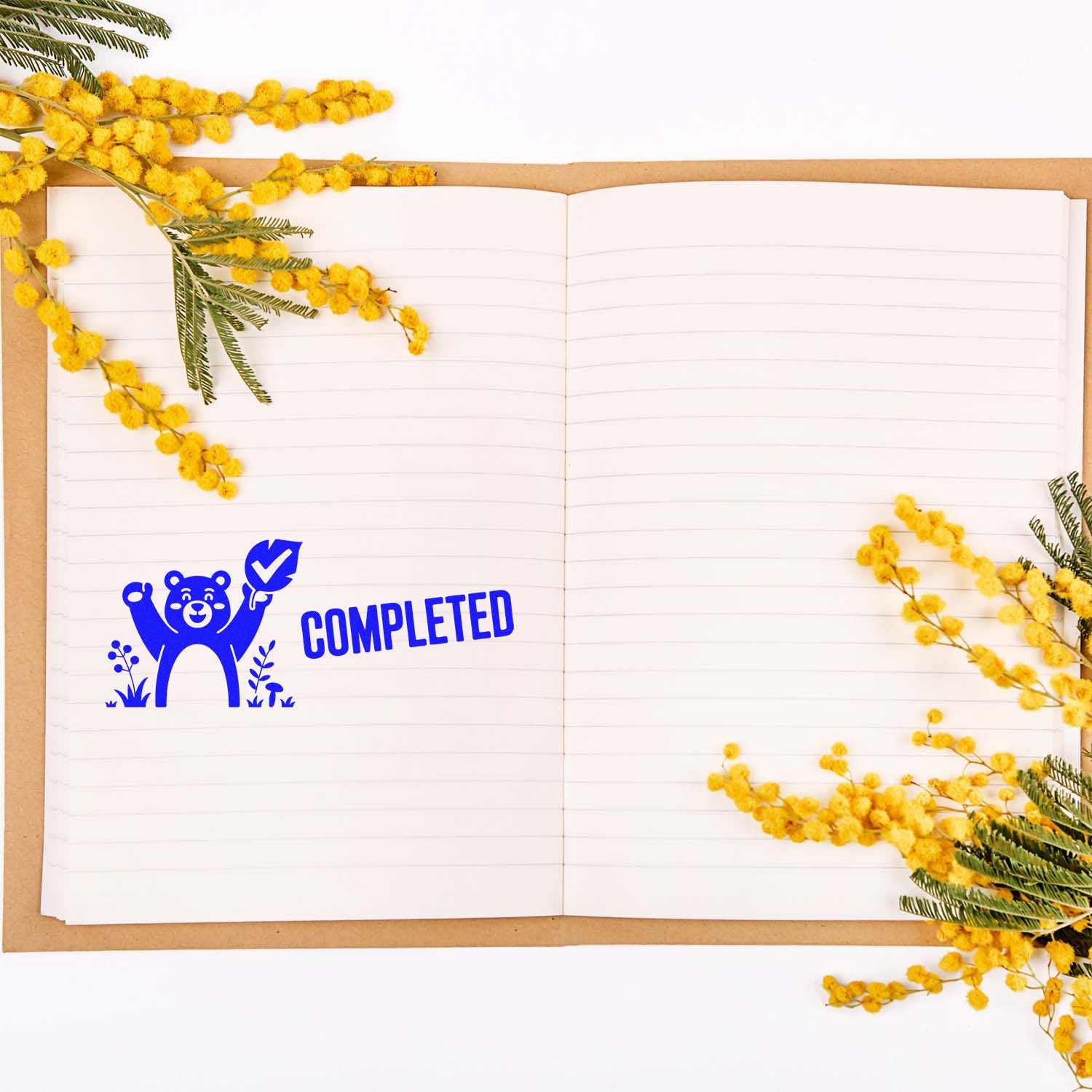 Completed rubber stamp with bear and checkmark on an open notebook, framed by yellow flowers for planner or task tracking use.