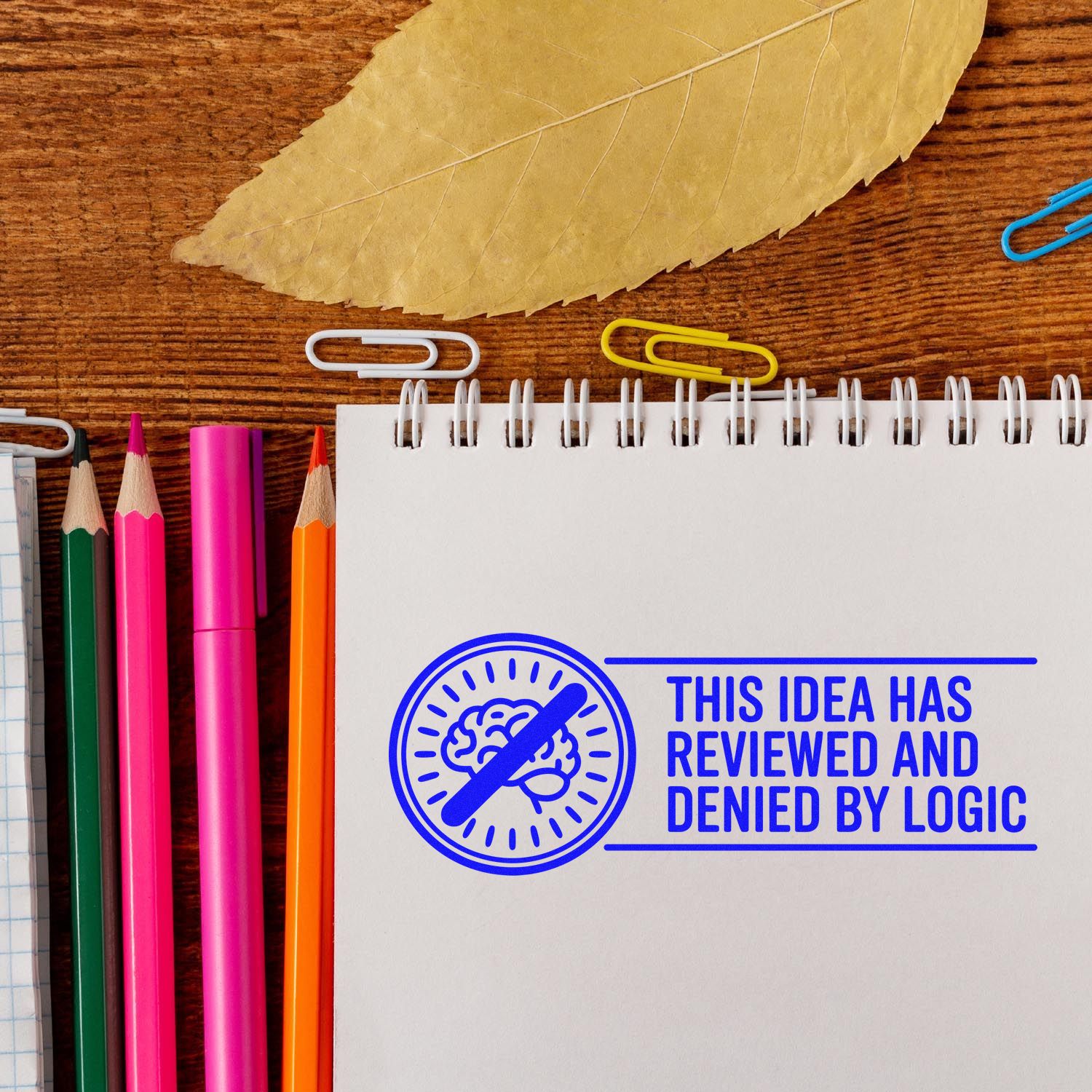 Blue custom rubber stamp on notebook says This idea has been reviewed and denied by logic with brain icon.