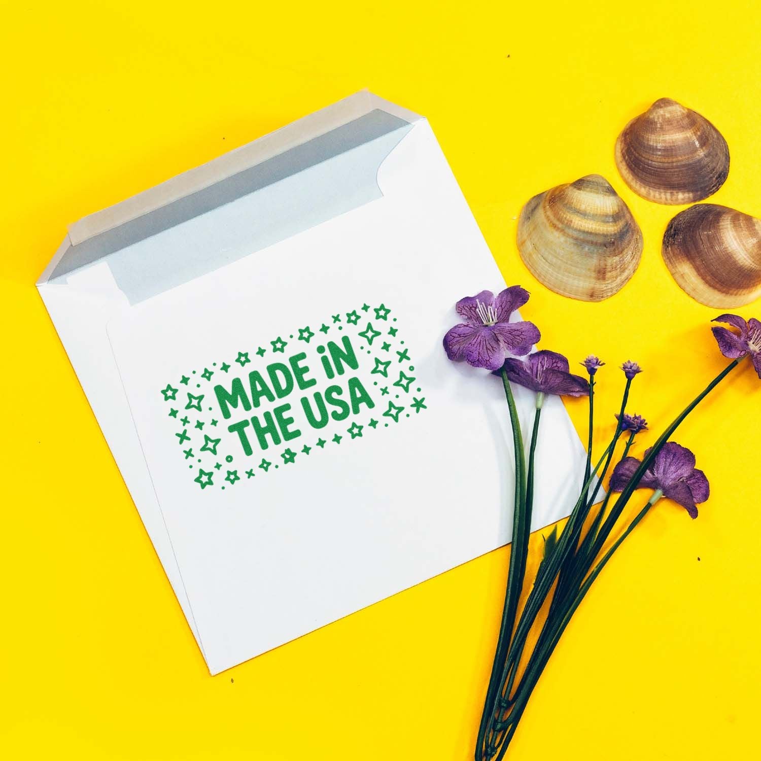 Made in the USA rubber stamp on a white envelope, with shells and purple flowers for custom packaging branding.