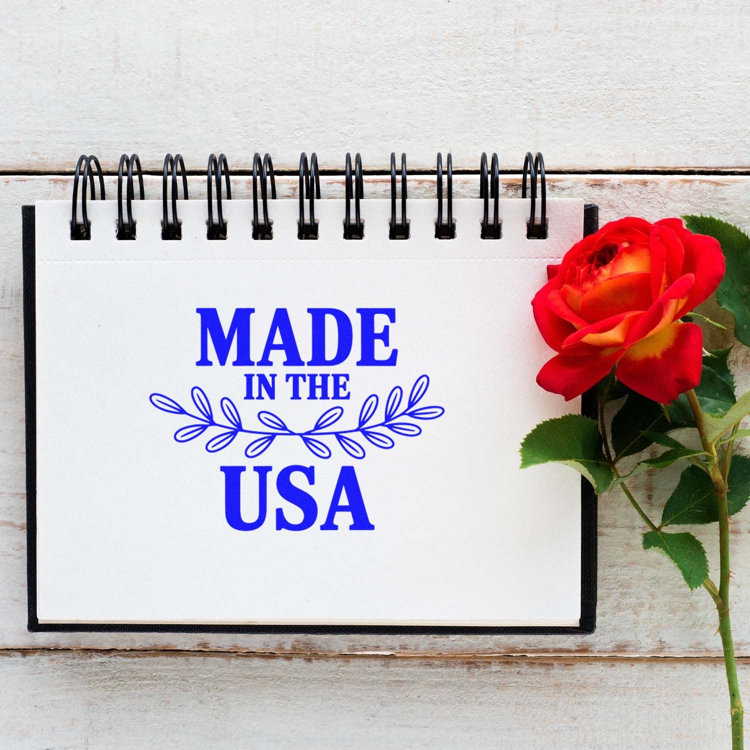 Made in the USA rubber stamp design in blue with floral accent, displayed on a notepad beside a red rose.