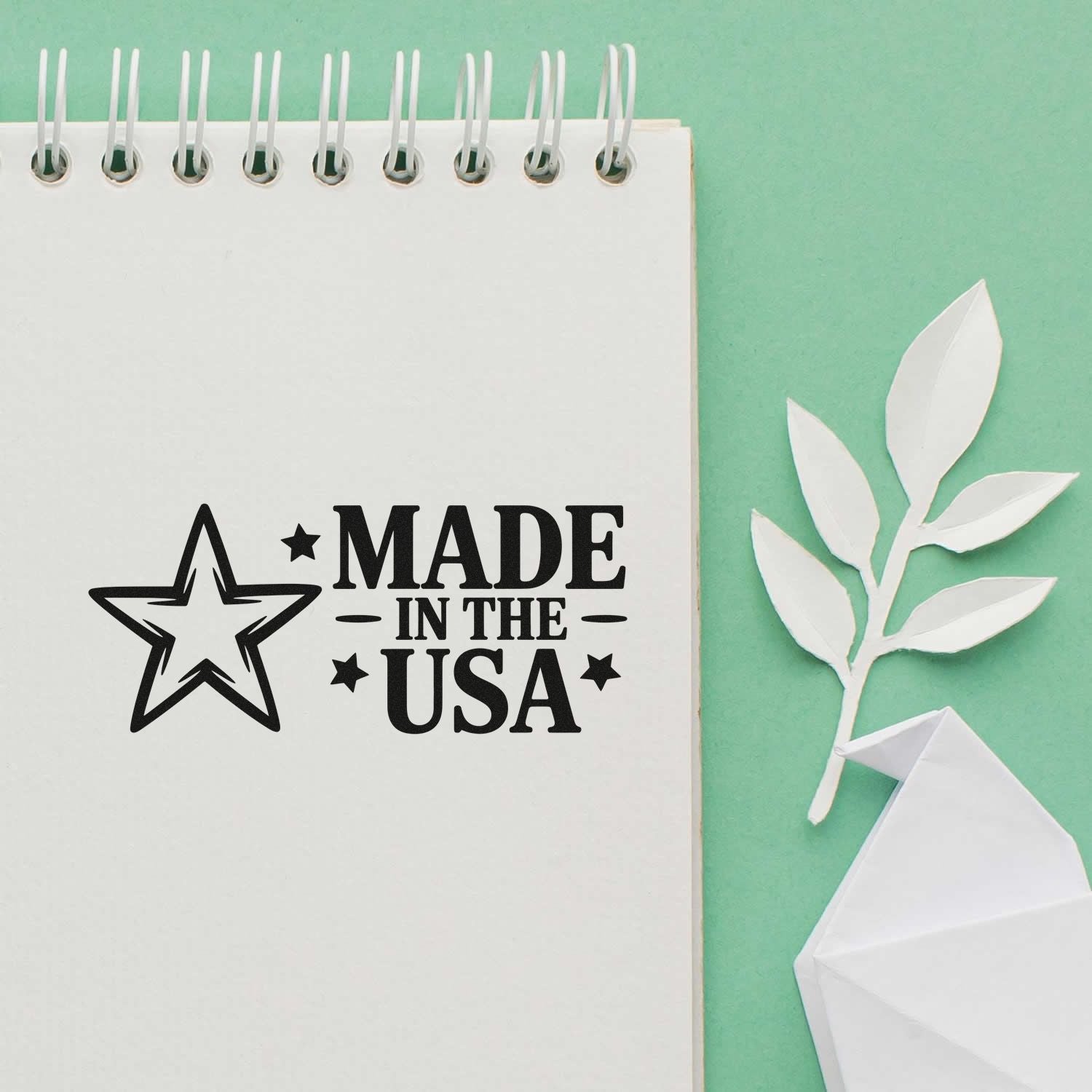 Made in the USA rubber stamp impression on notebook paper, shown with paper craft leaves and origami on a mint background.
