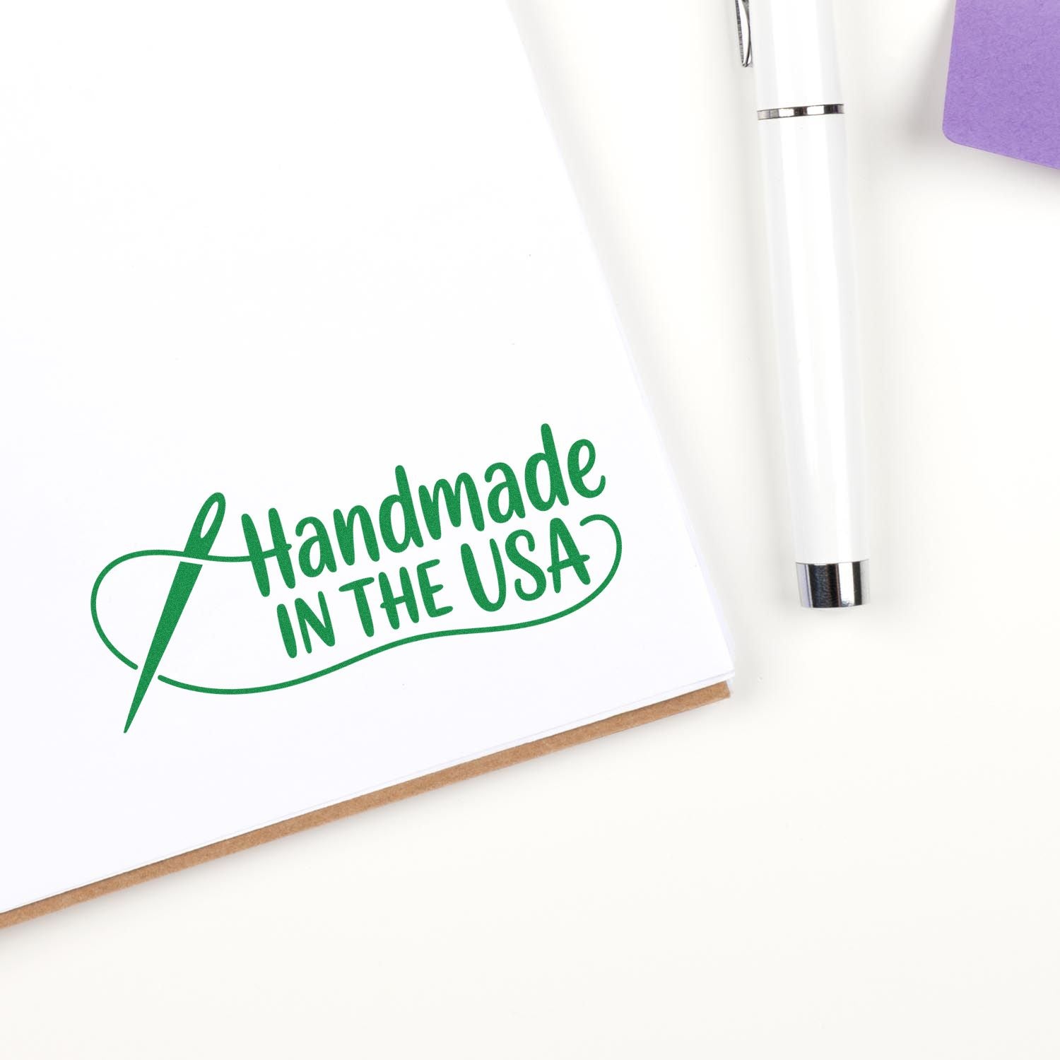 Green Handmade in the USA rubber stamp on notebook with pen, ideal for handmade product packaging and branding.