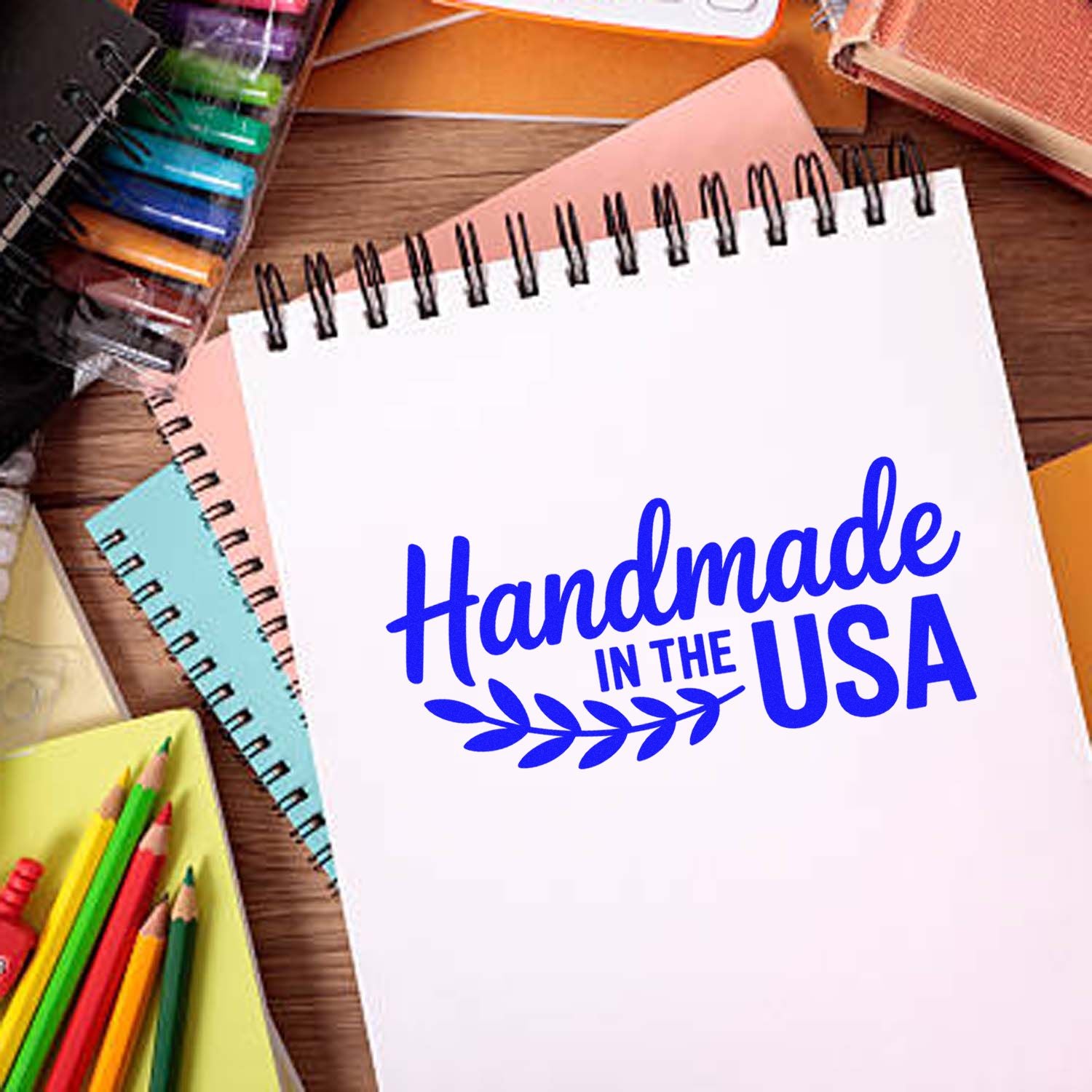Handmade in the USA rubber stamp design on a blank notebook, surrounded by colorful craft and stationery supplies.