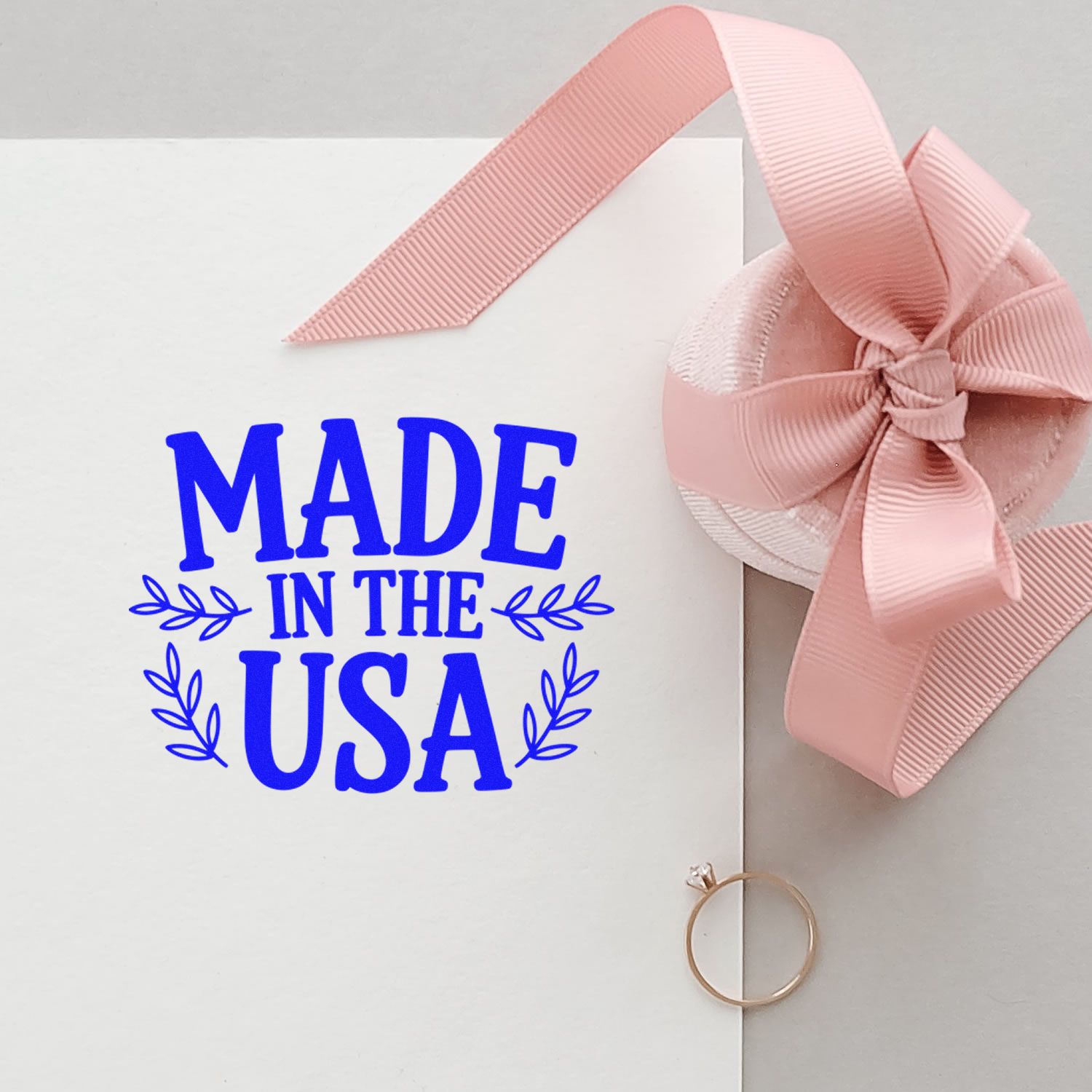 Made in the USA rubber stamp imprint on white card with pink bow, ideal for handmade product packaging and crafts.