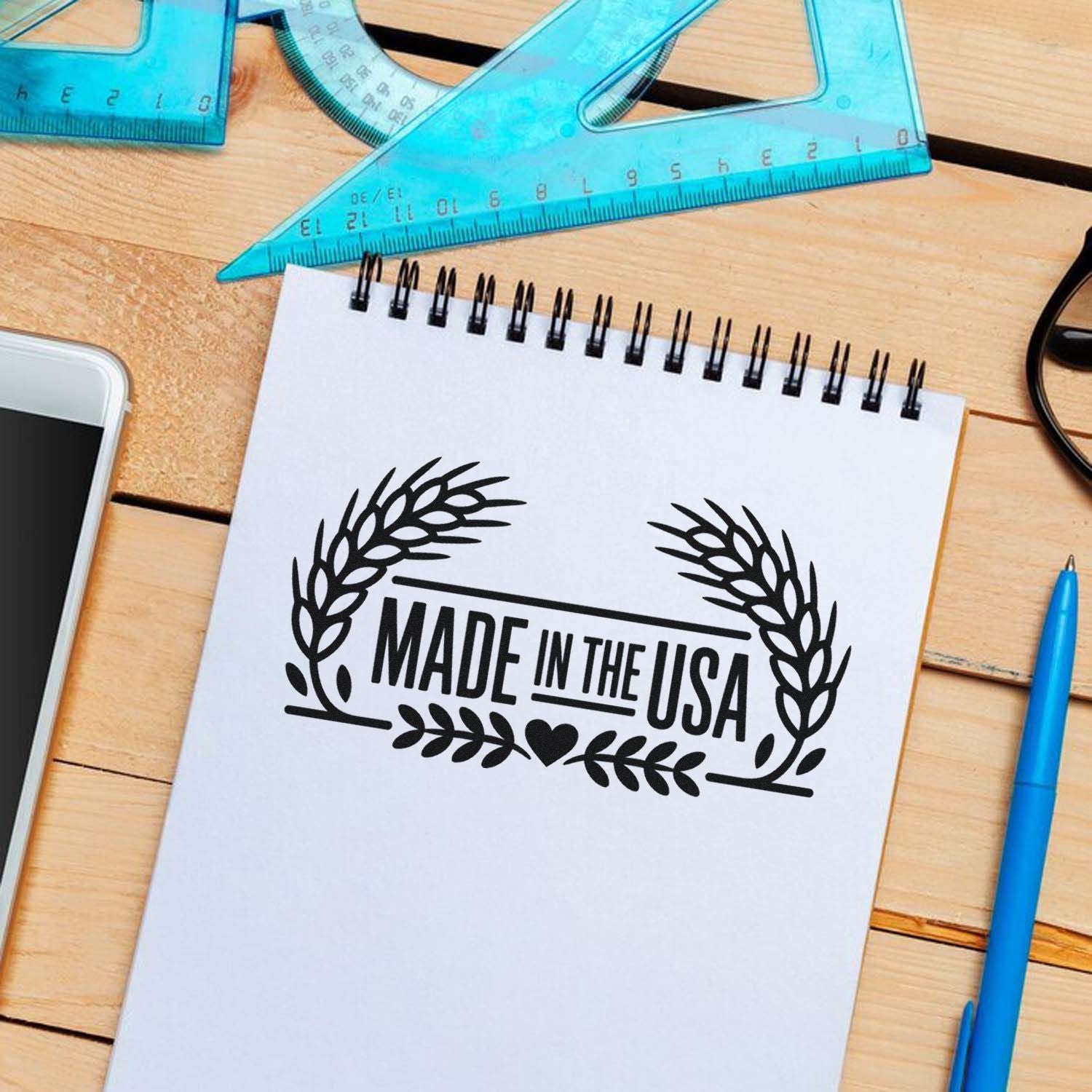 Made in the USA rubber stamp impression on notebook paper, displayed with drafting tools on a wooden desk.