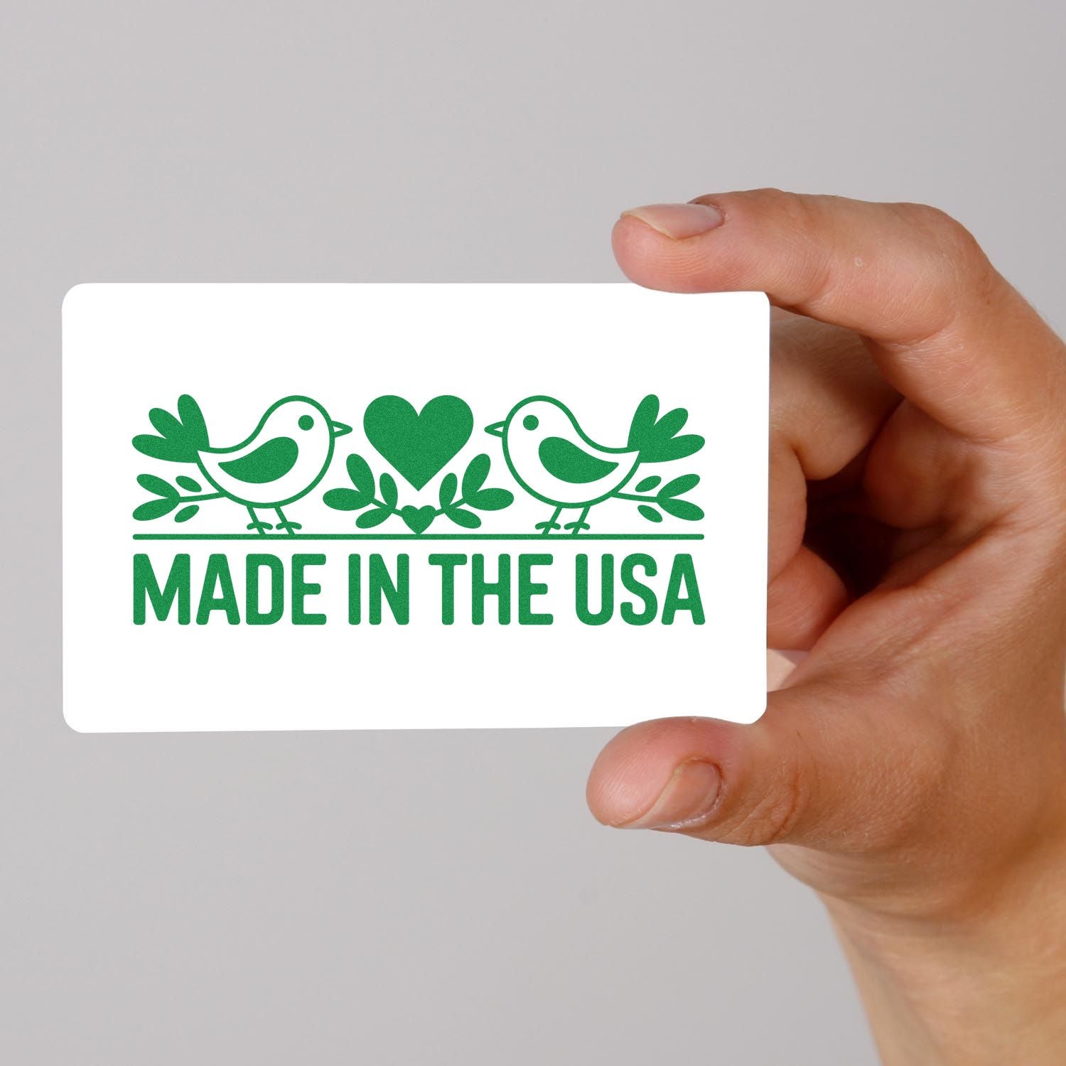 Hand holding a Made in the USA rubber stamp design with birds, heart, and leaves in green ink.