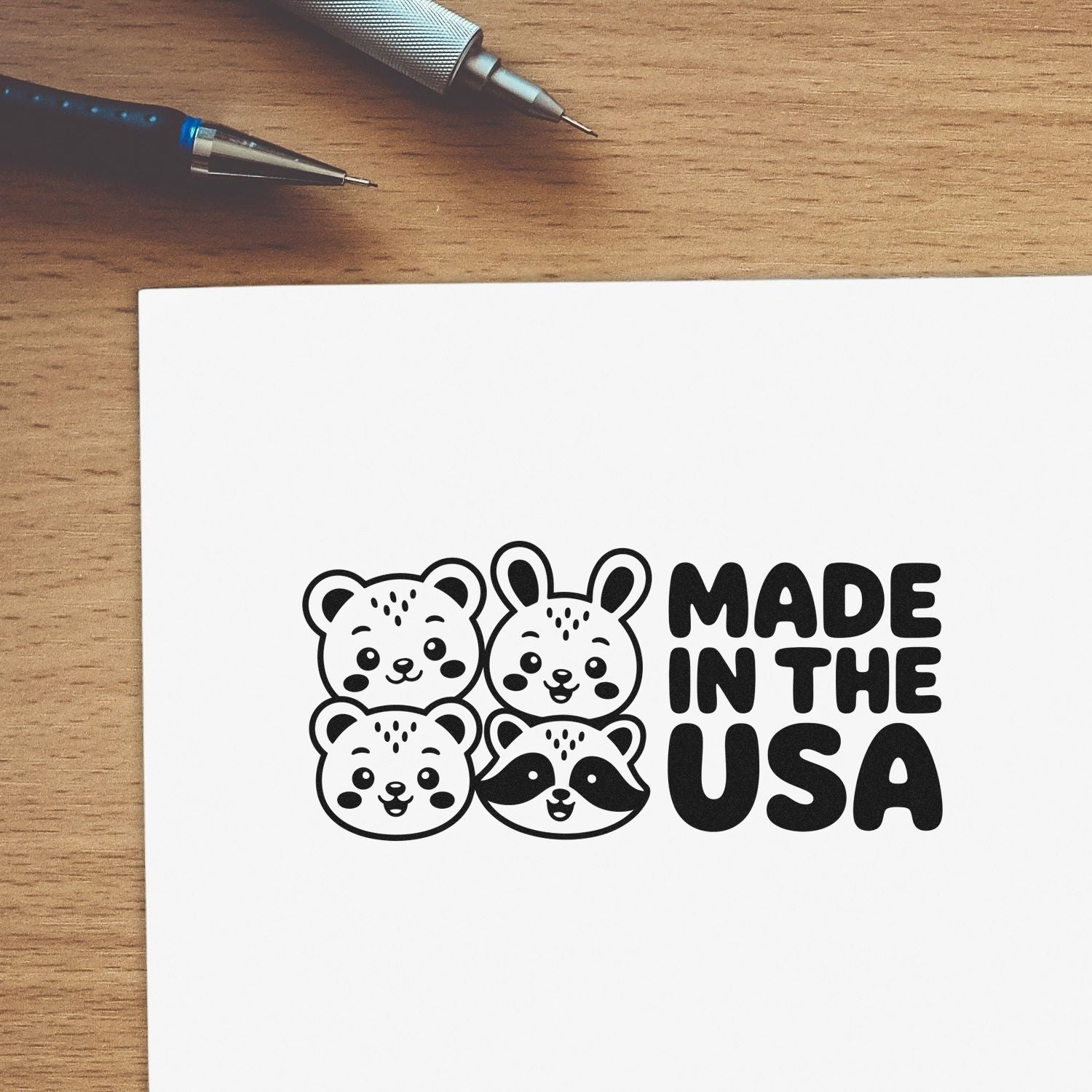 Made in the USA rubber stamp design with cute bear, bunny, and raccoon faces on paper beside drafting pens.