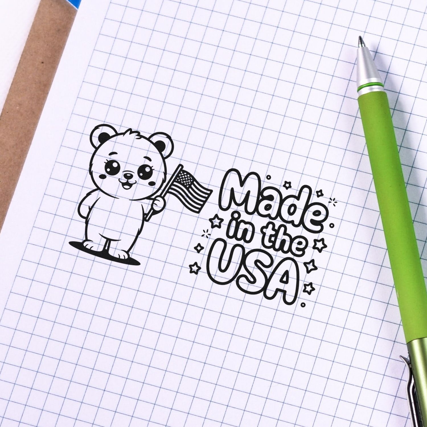 Patriotic rubber stamp design with bear holding U.S. flag and Made in the USA text on graph paper.