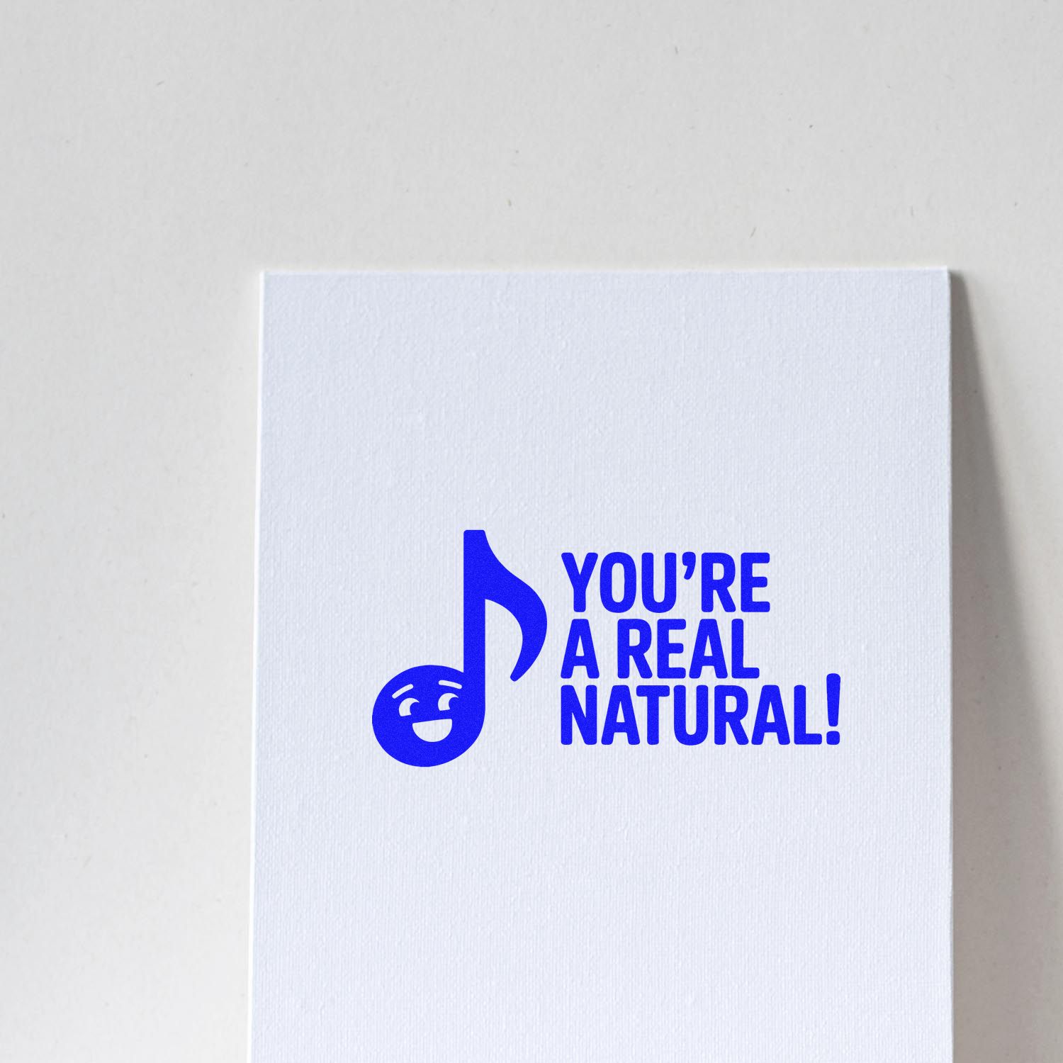 Custom rubber stamp design with musical note smiley and text Youre a Real Natural! in blue on white paper.