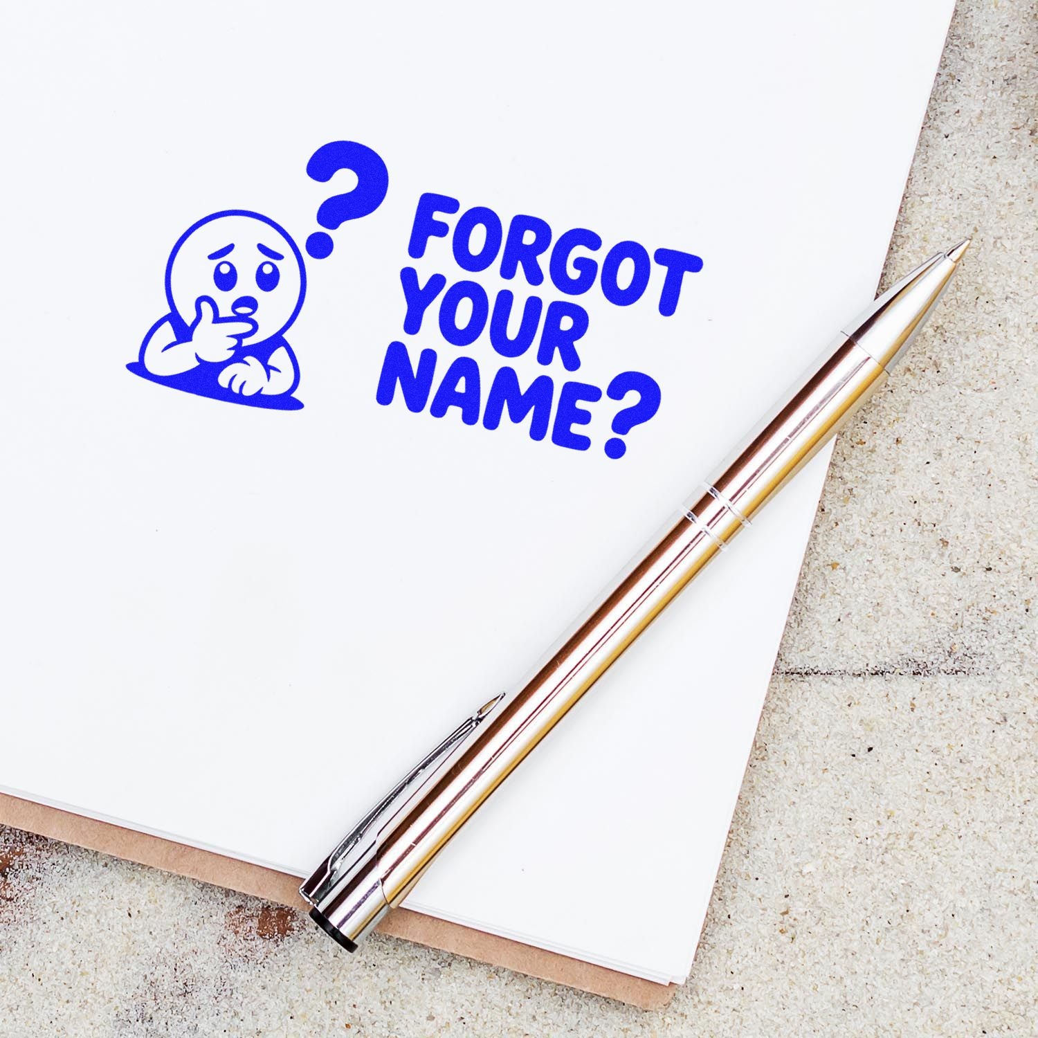 Blue rubber stamp design reading Forgot Your Name? with confused character icon on a notebook page beside a pen.