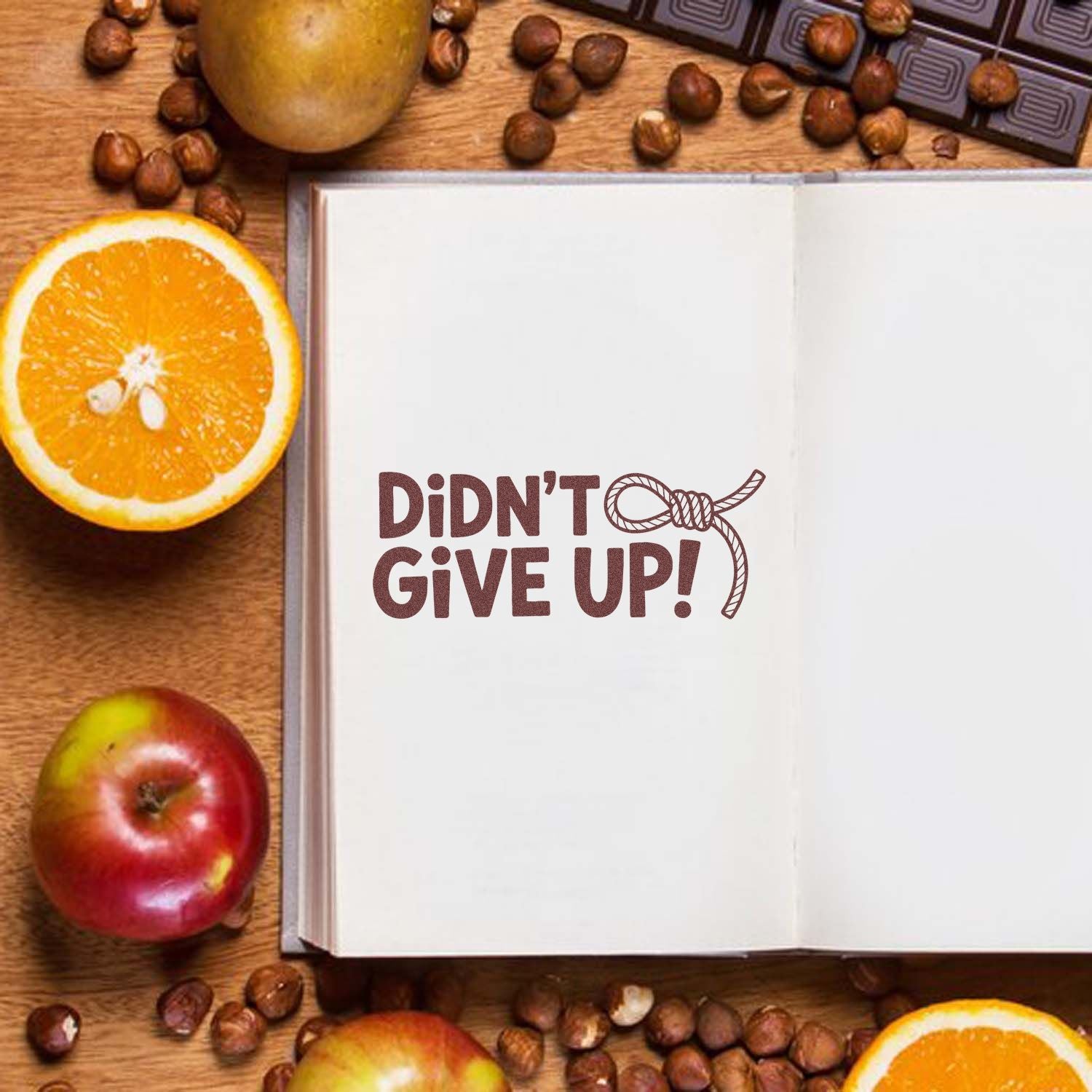 Motivational rubber stamp design reading Didnt Give Up! on an open notebook, surrounded by fruit and coffee beans.