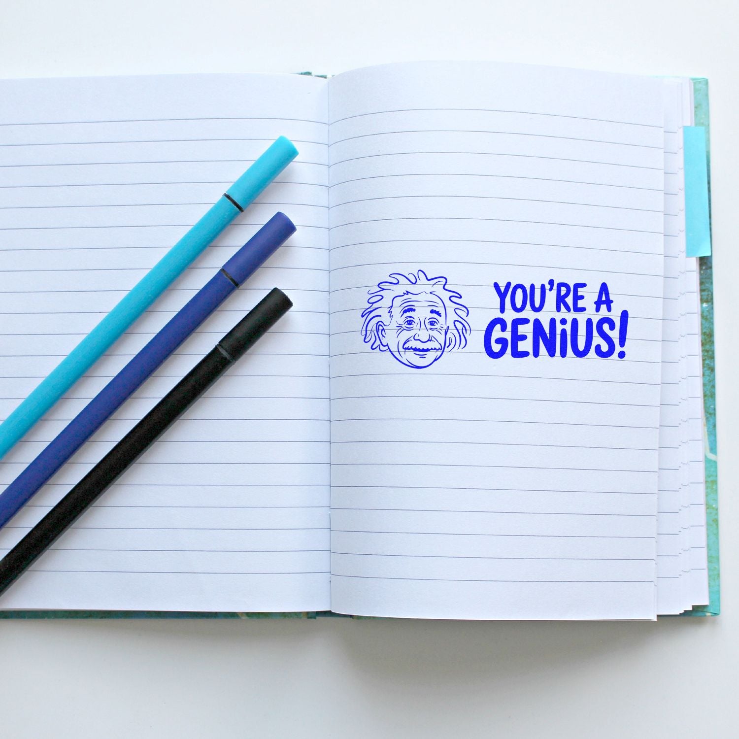 Youre a Genius rubber stamp impression on notebook pages, ideal for teacher reward and motivational student feedback.