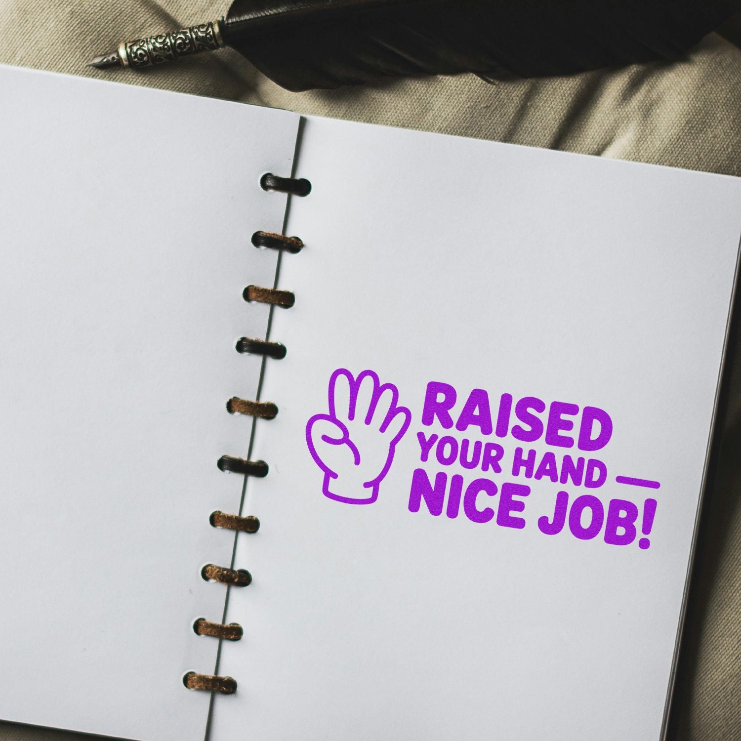 Purple classroom rubber stamp saying Raised Your Hand Nice Job! on a notebook page for student recognition.