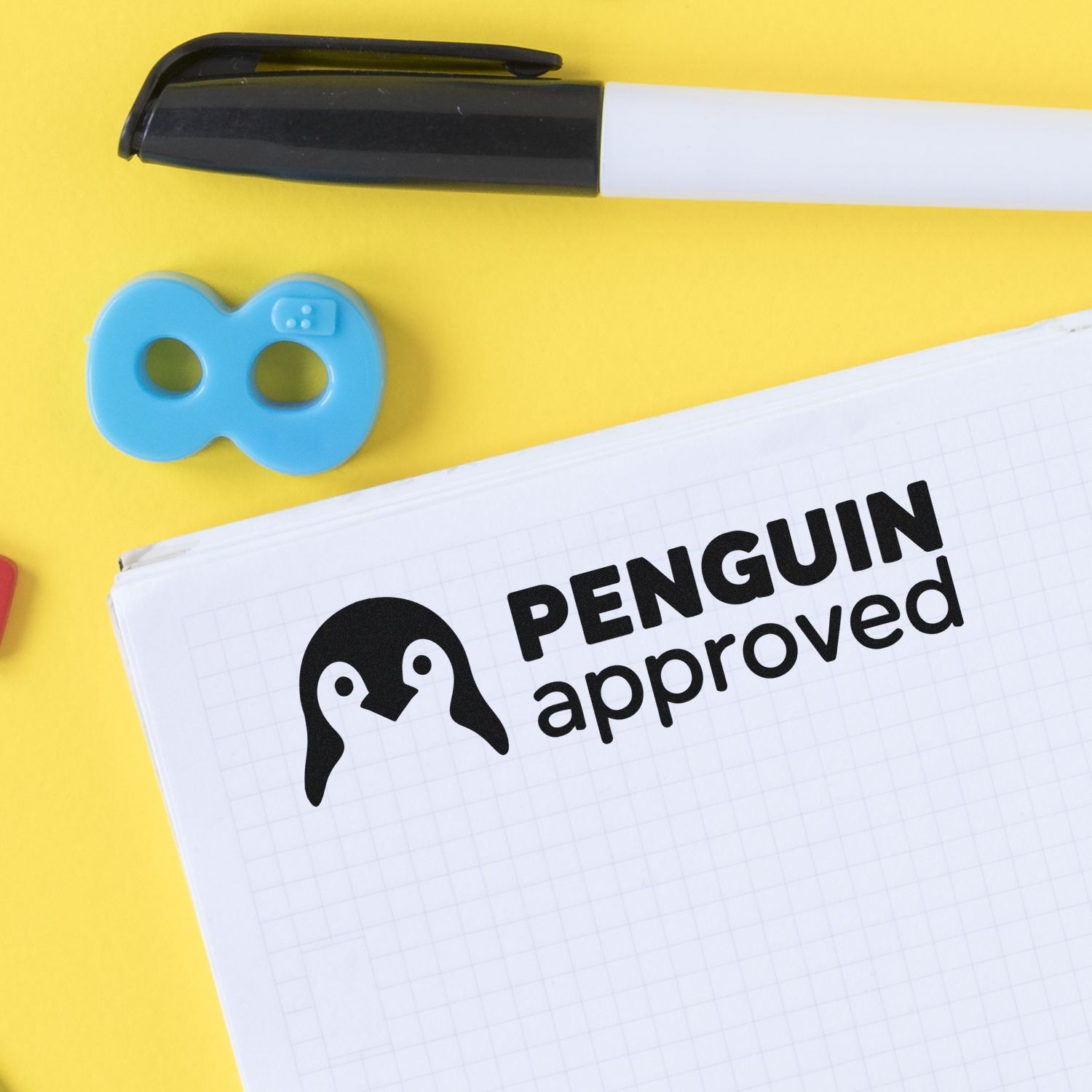Penguin approved rubber stamp mockup on notebook with marker and stamp accessory on yellow background.