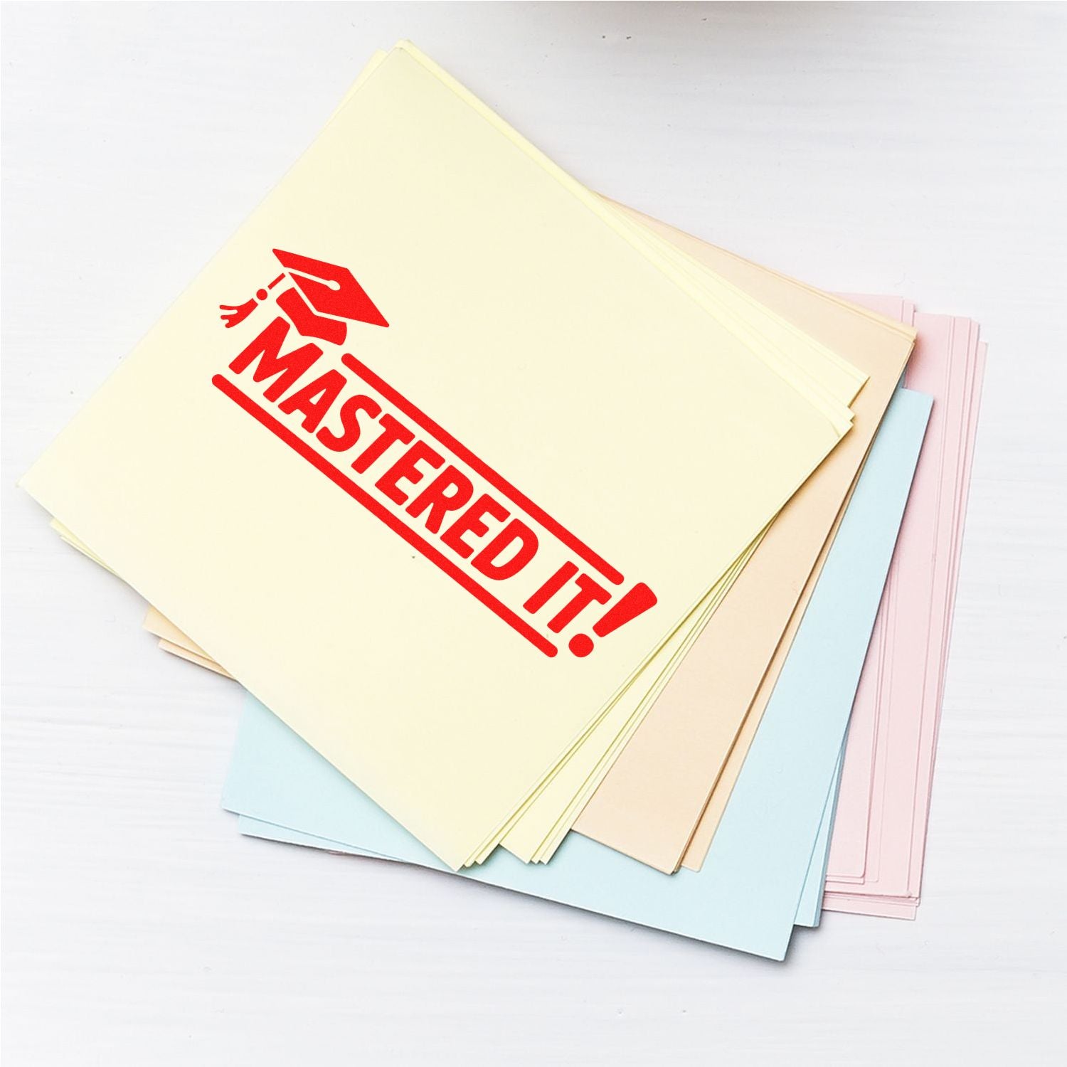 Red Mastered It! rubber stamp on pastel paper stack, ideal for teacher grading and classroom reward marking.