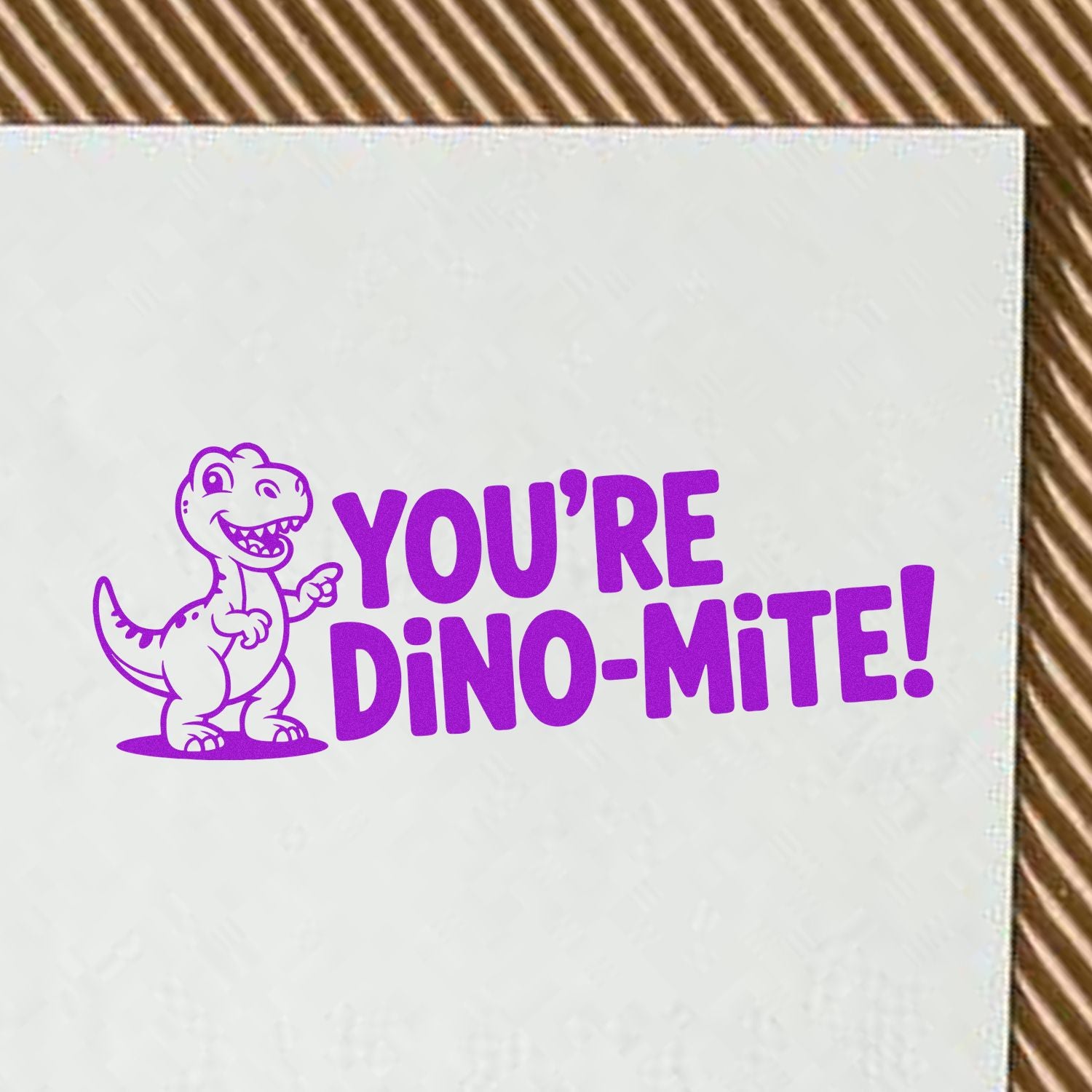 Purple rubber stamp impression with cartoon dinosaur and Youre Dino-Mite! text for kids crafts and greeting cards.