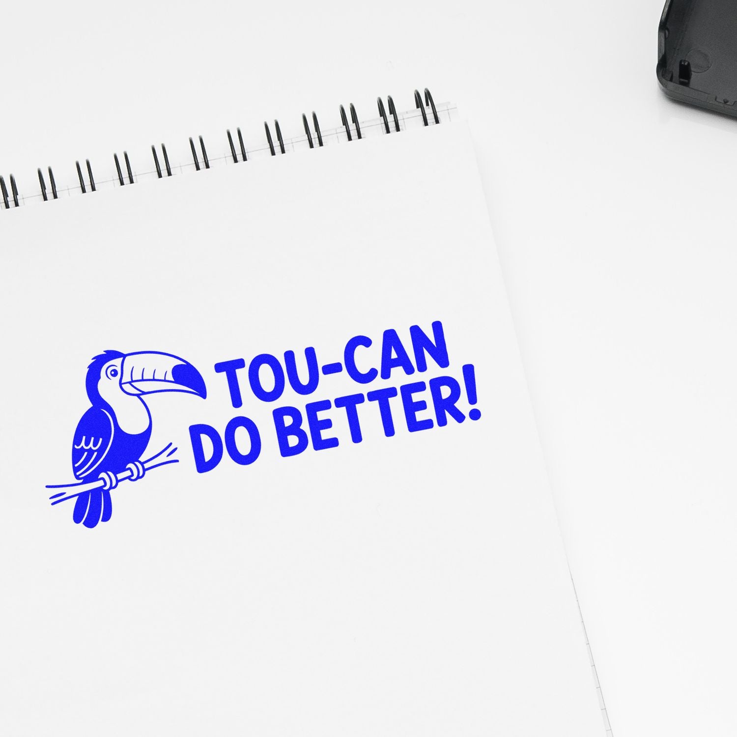 Toucan-themed rubber stamp design with Tou-can do better! slogan on a notebook page.