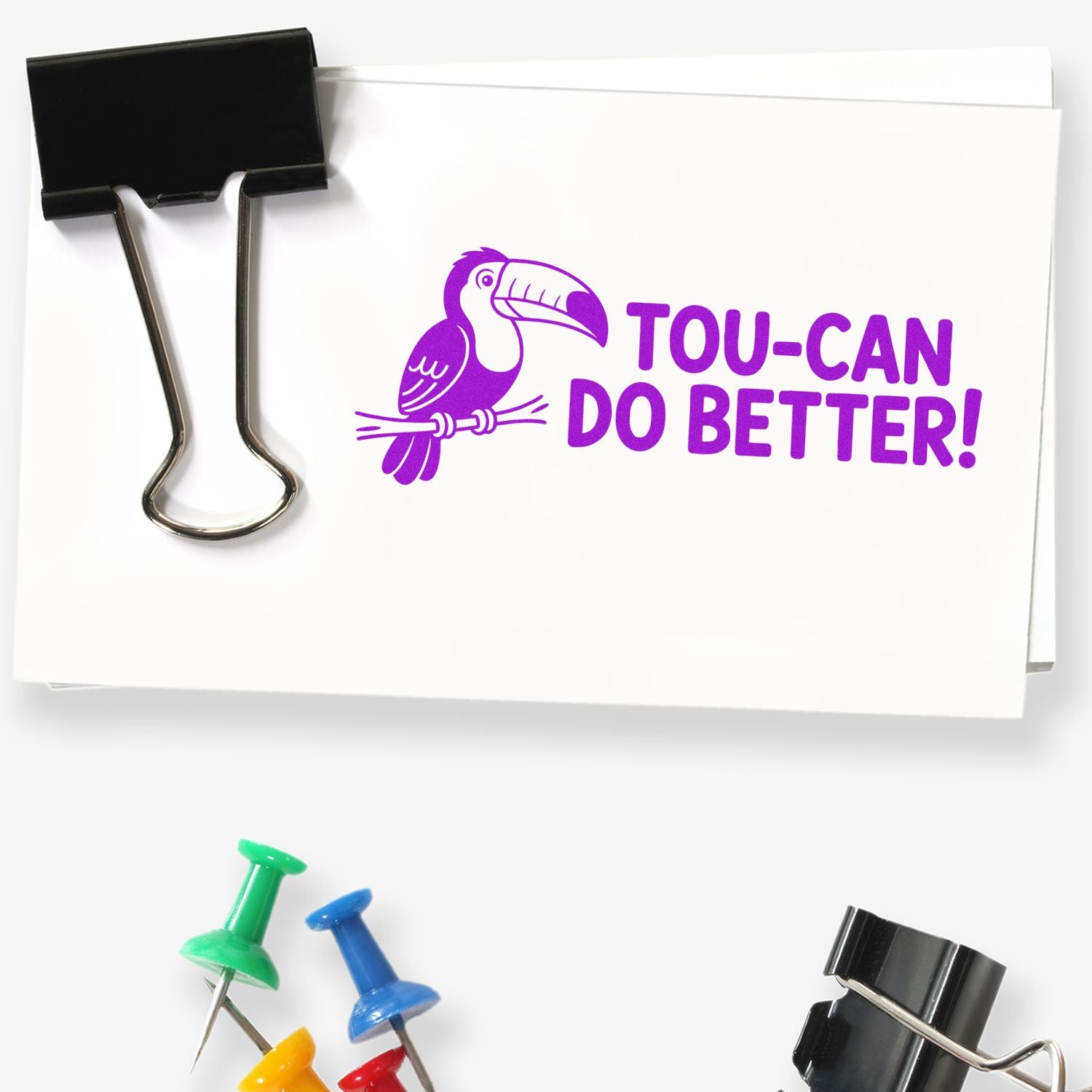 Custom rubber stamp sample with toucan logo and Tou-can Do Better! on white paper clipped with a binder clip