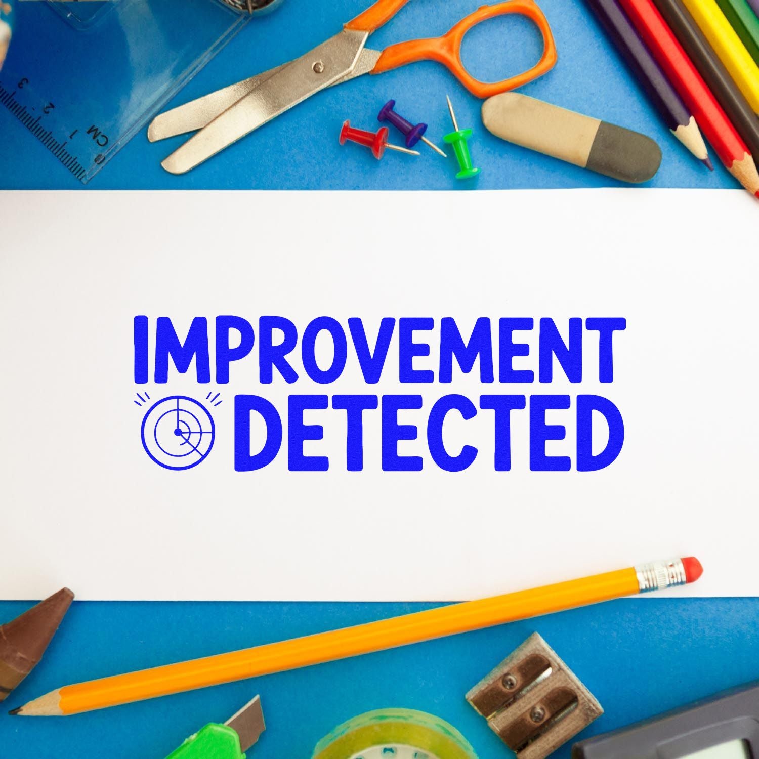 Improvement Detected rubber stamp for teacher feedback, shown on white paper with school supplies.
