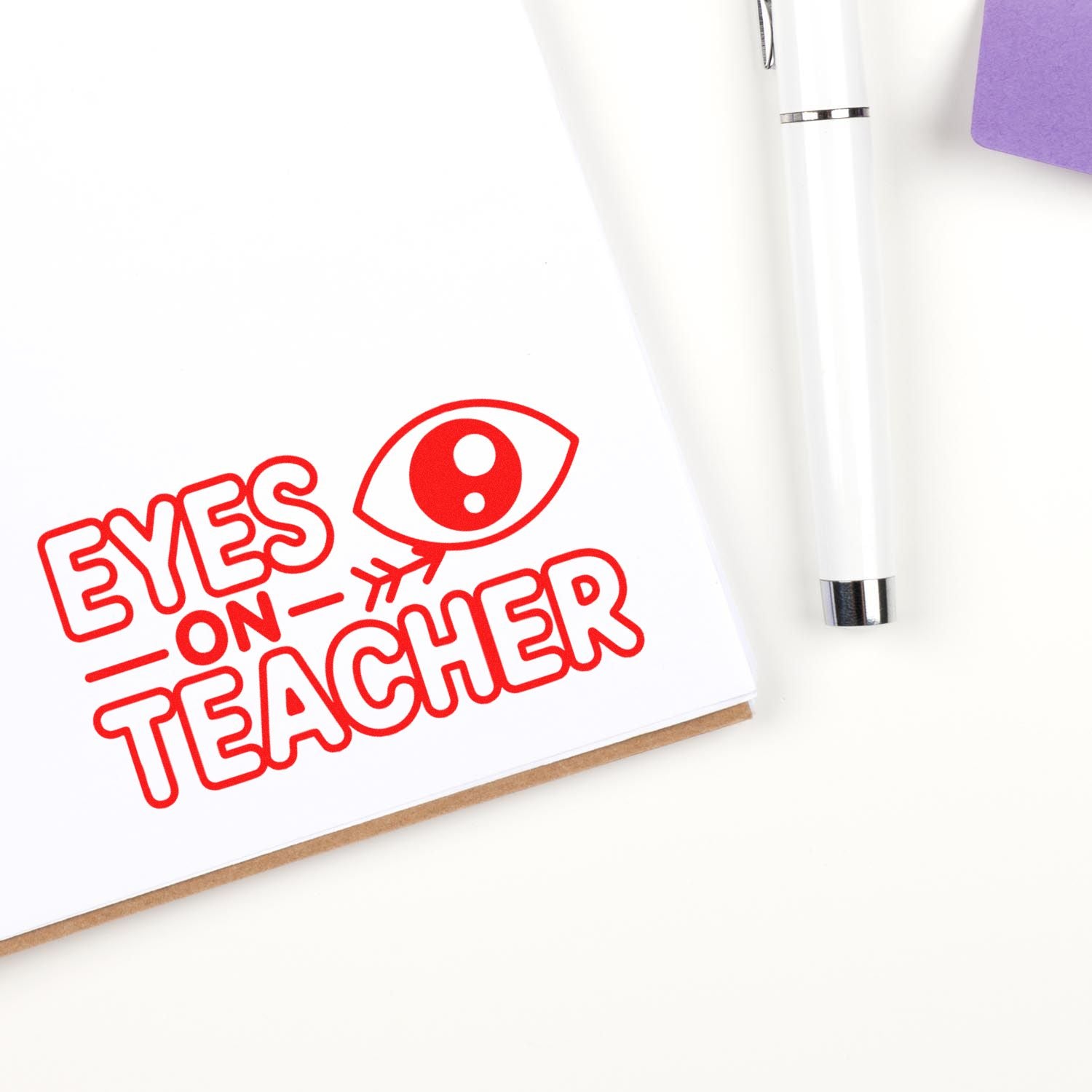 Eyes on Teacher rubber stamp design for classroom behavior reminders, stamped in red on notebook beside a pen.