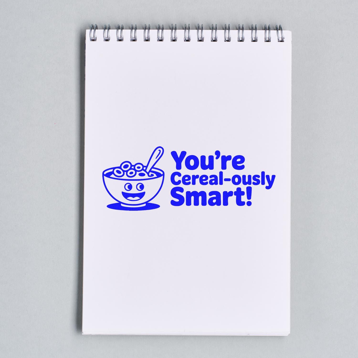 Blue rubber stamp impression on notebook reading Youre cereal-ously smart! with smiling cereal bowl design.
