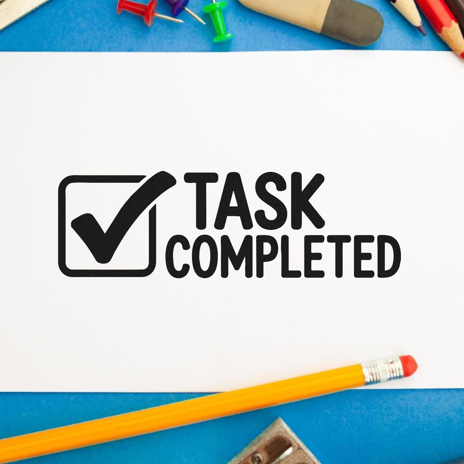 Task completed rubber stamp with checkmark icon on paper, surrounded by school supplies for organizing work and projects.