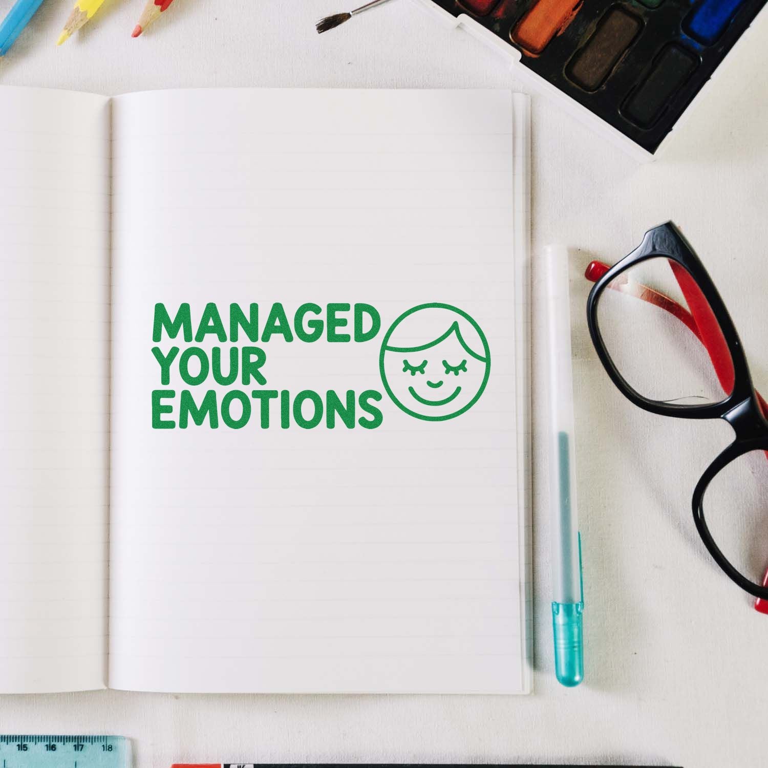 Rubber stamp design reading Managed Your Emotions with smiling face on an open notebook, surrounded by art supplies